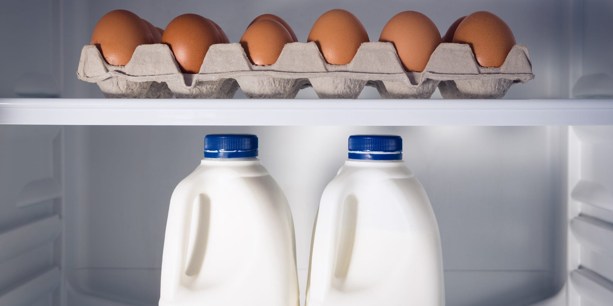 A carton of eggs and two bottles of milk inside of a refrigerator