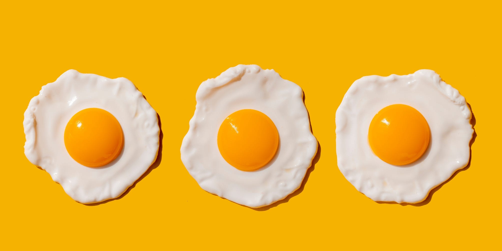 Three fried eggs against a yellow background.