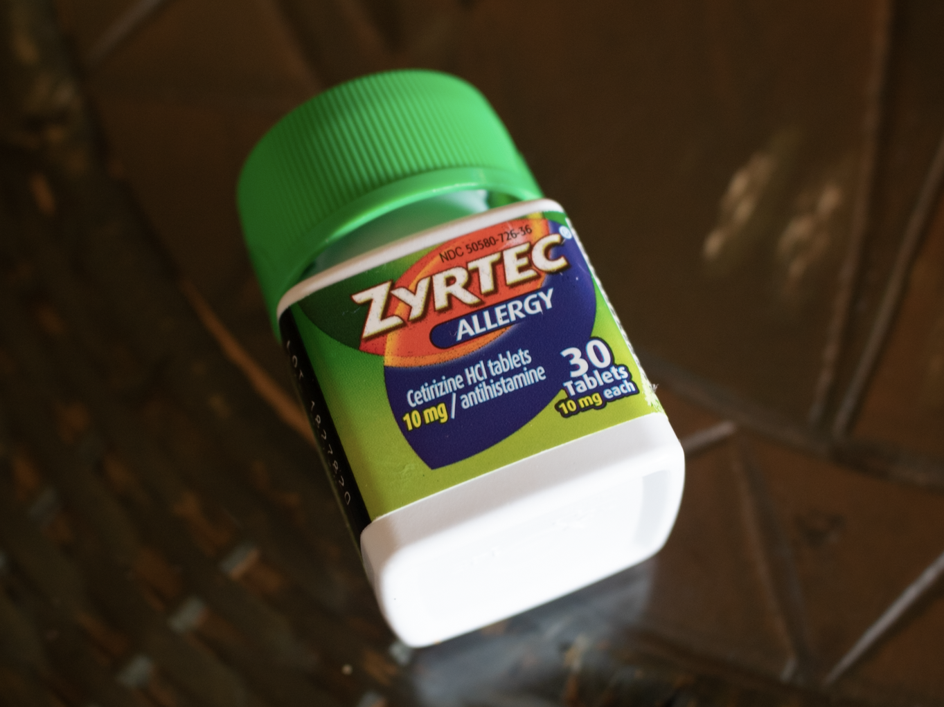 A green and white bottle of Zyrtec on a brown table