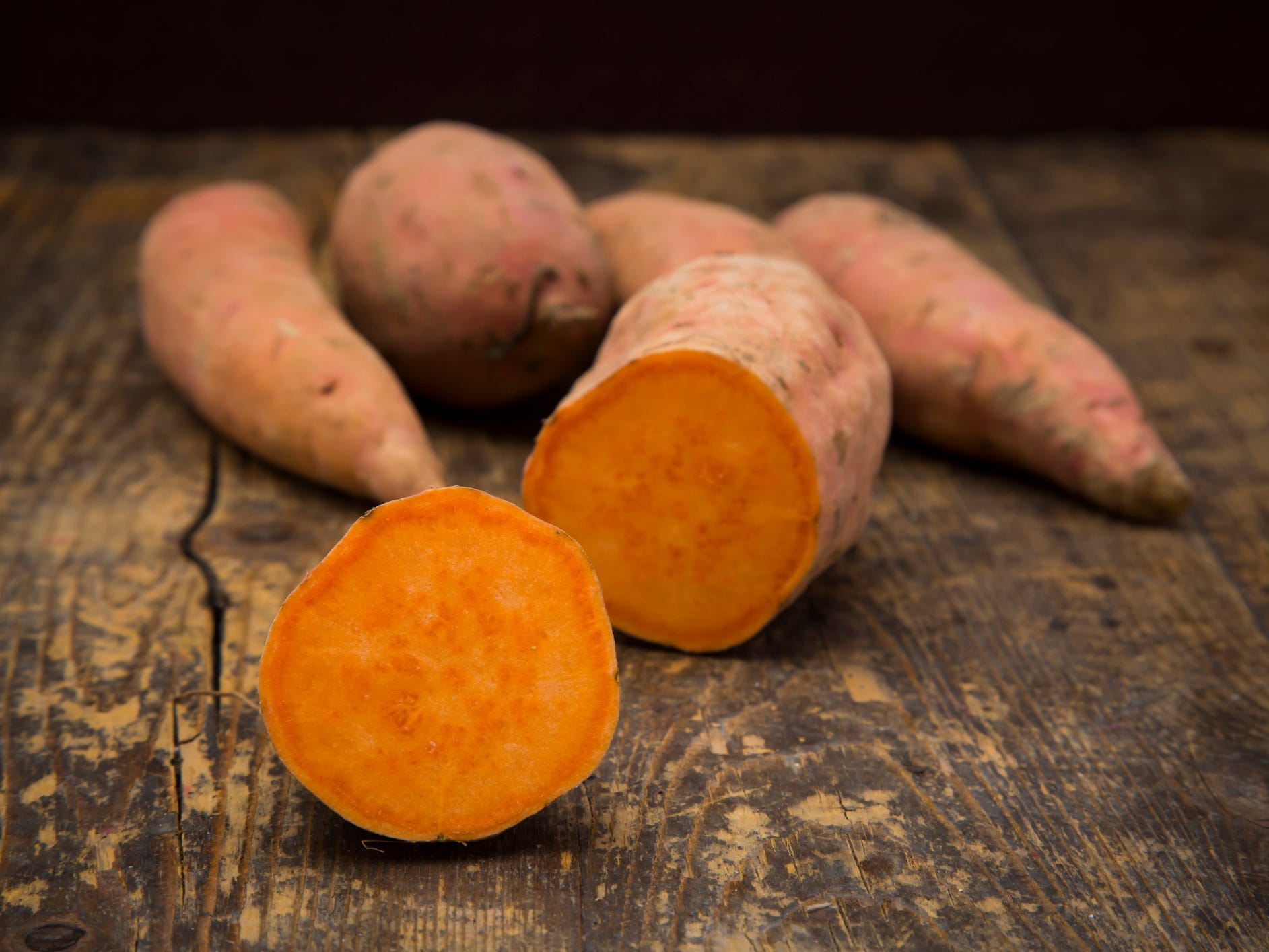 Sliced and whole sweet potatoes on dark wood.