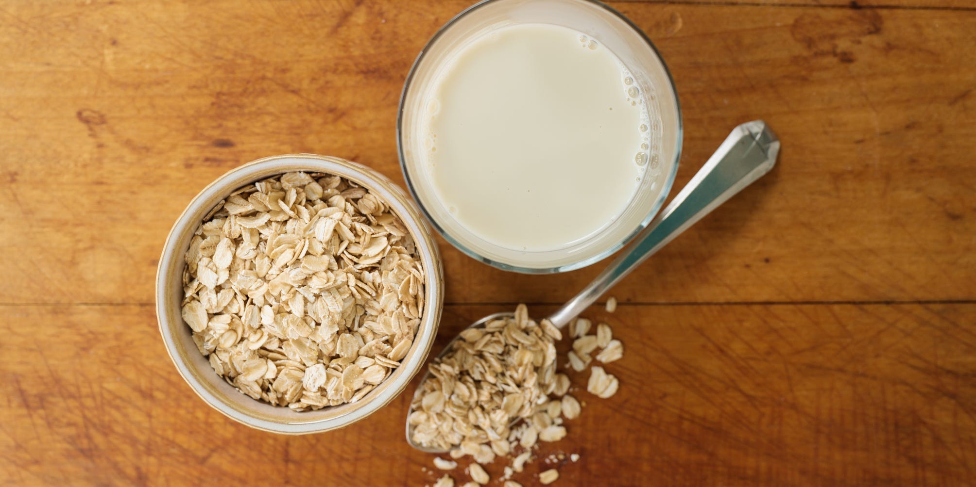 Overhead shot of a jar of oats, a spoon full of oats, and a glass of milk.