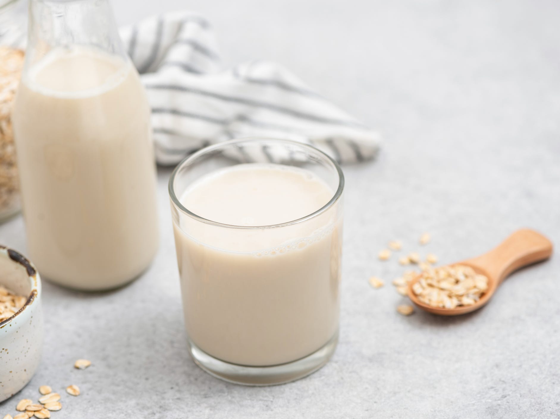 Vegan oat milk in glass with a spoon of oats in the background.