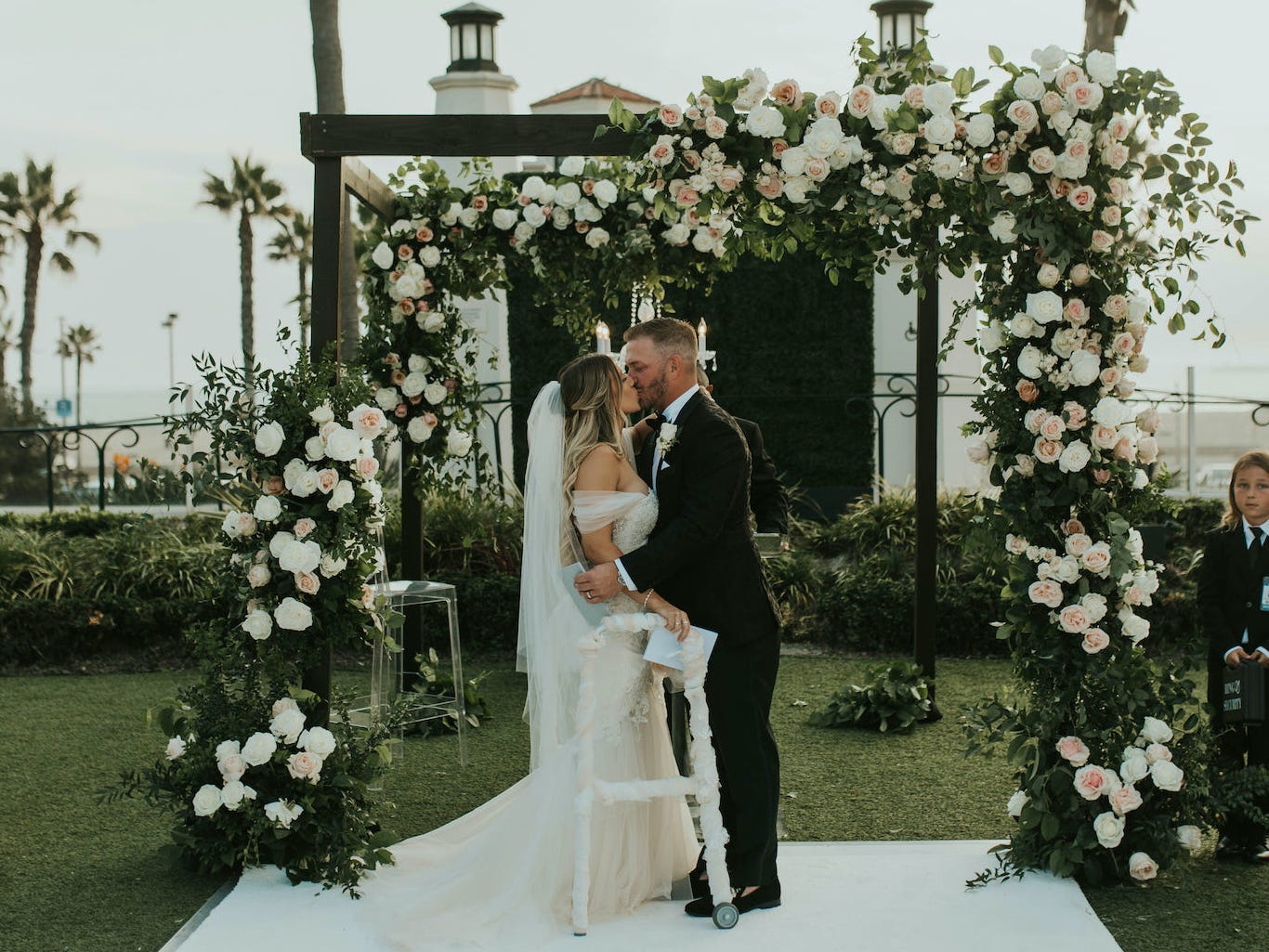 A groom kisses his bride at their flower-covered wedding altar.