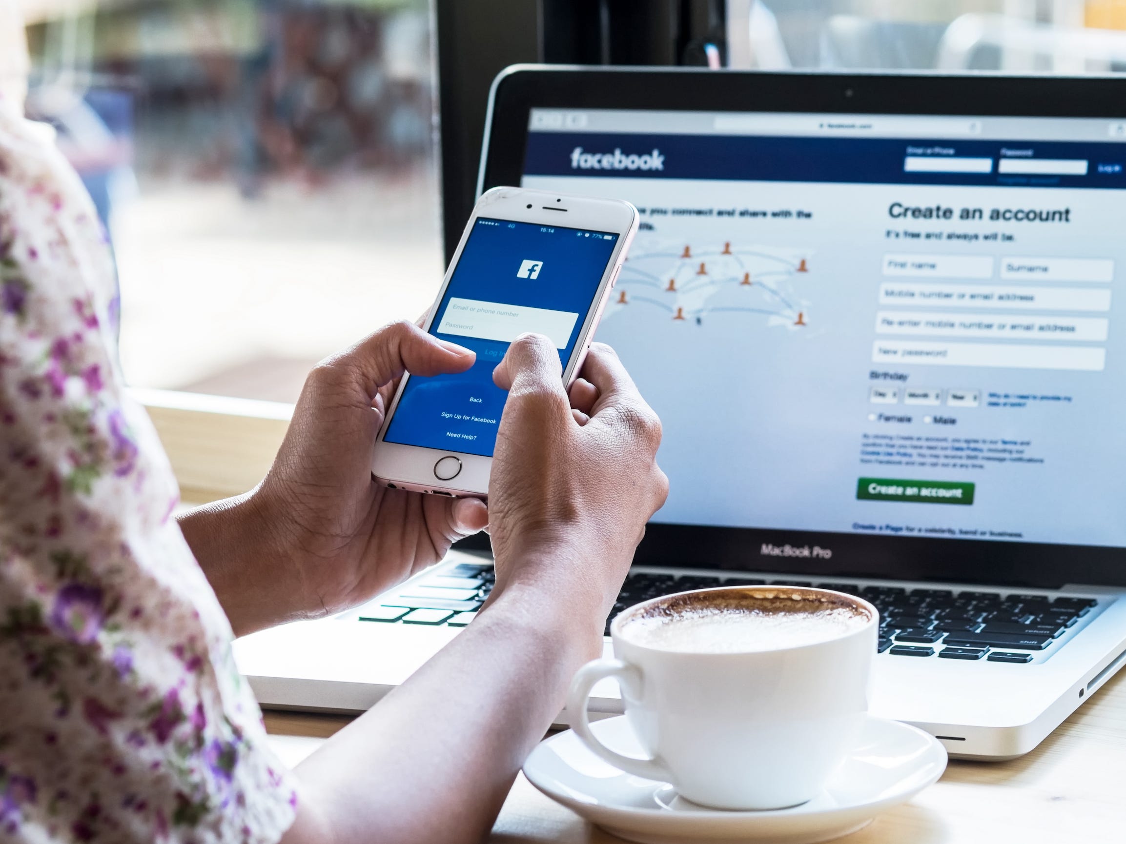 A person using the Facebook app on their smartphone in front of a laptop, which is also running Facebook.