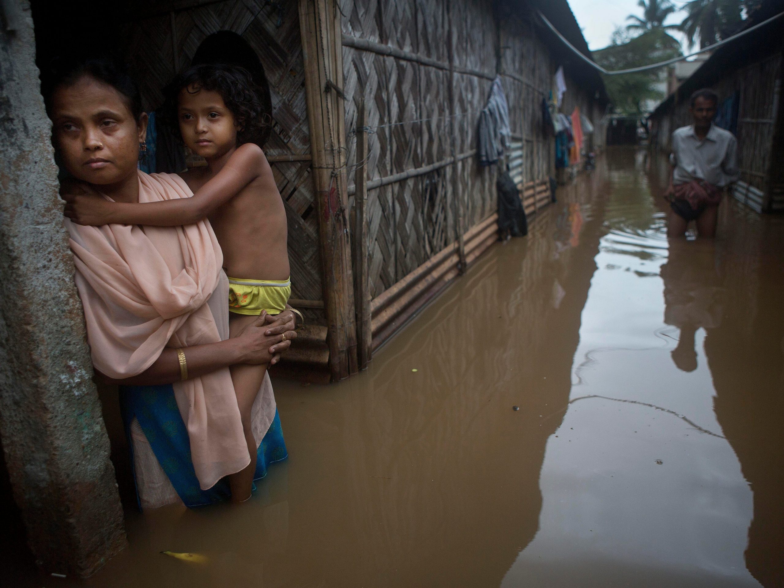 In this Sept. 25, 2015, file photo, a woman holds her daughter stands awaiting her husband who went to collect drinking water after flood waters enter their house following heavy monsoon rains in Gauhati, India.