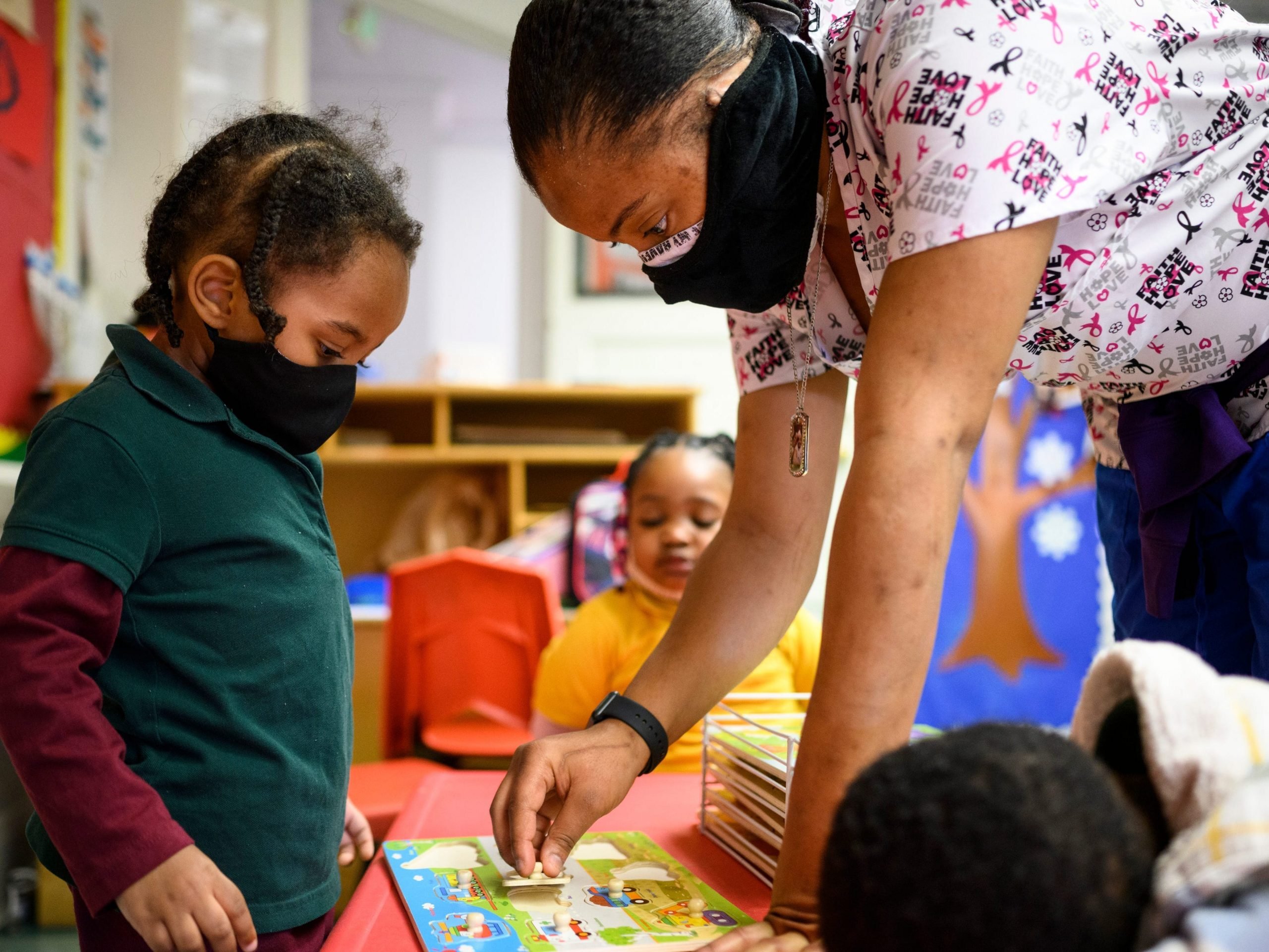 Shanikia Johnson, a three-year-olds teacher, helps Magjor Jones clean up a puzzle at Little Flowers Early Childhood and Development Center in the Sandtown-Winchester neighborhood of Baltimore, Maryland on January 12, 2021.