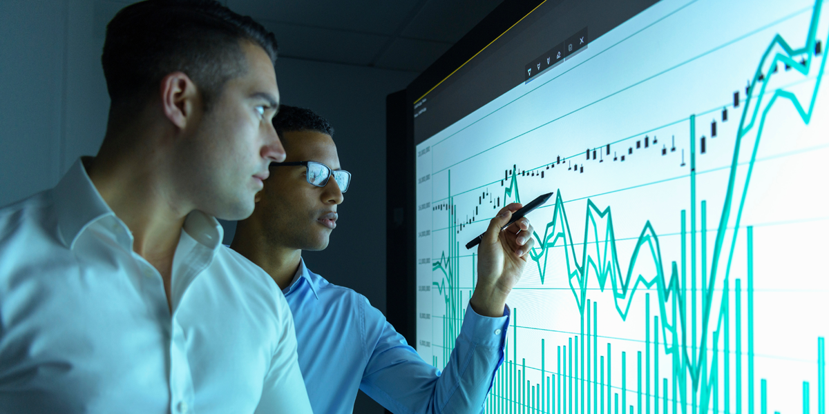 A photo of two men studying graphs on an interactive screen.