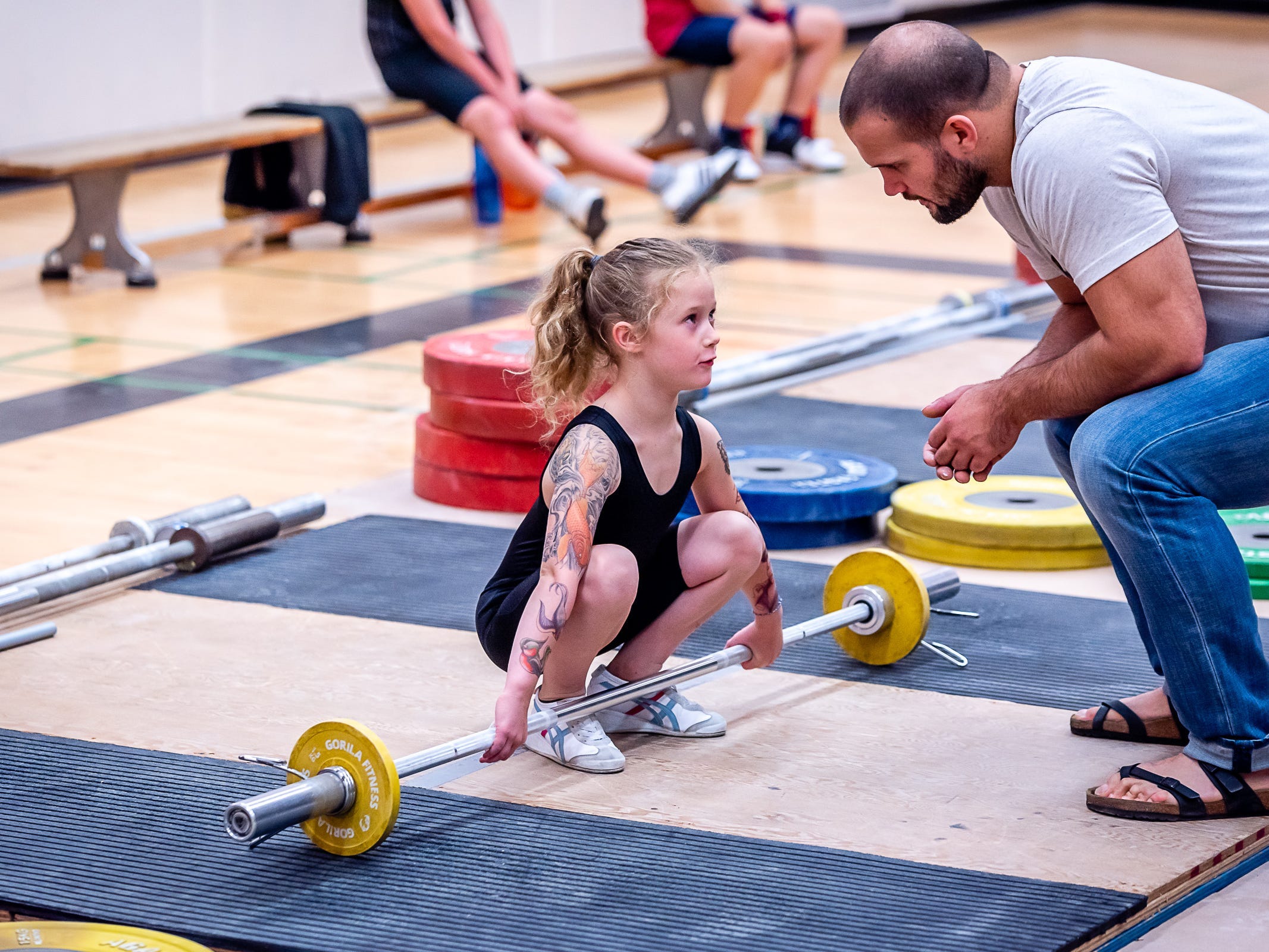 An eight-year-old girl being coaching on Olympic lifting technique with a barbell