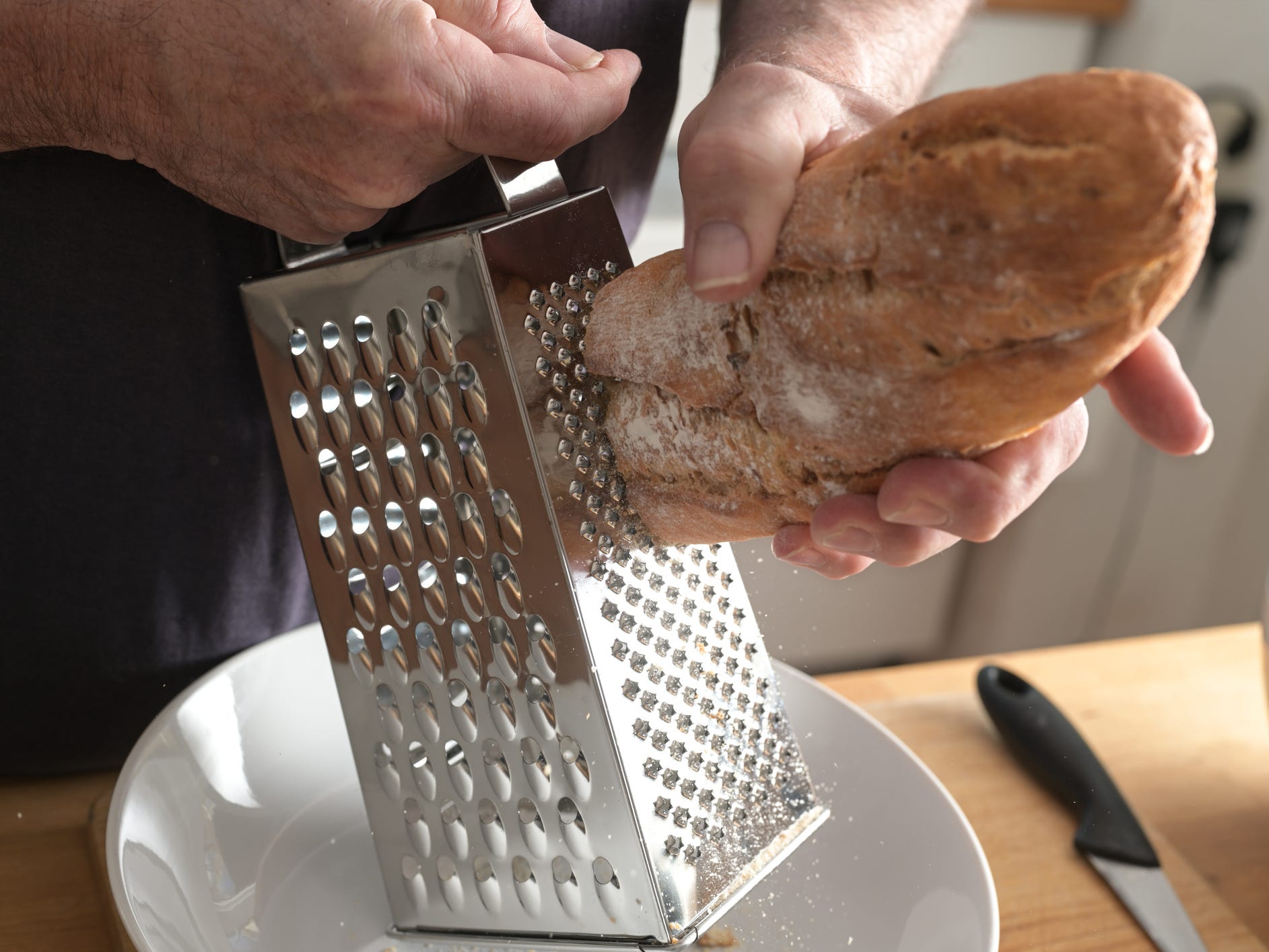 Hands of a man are grating hard bread on a grater to get breadcrumbs.