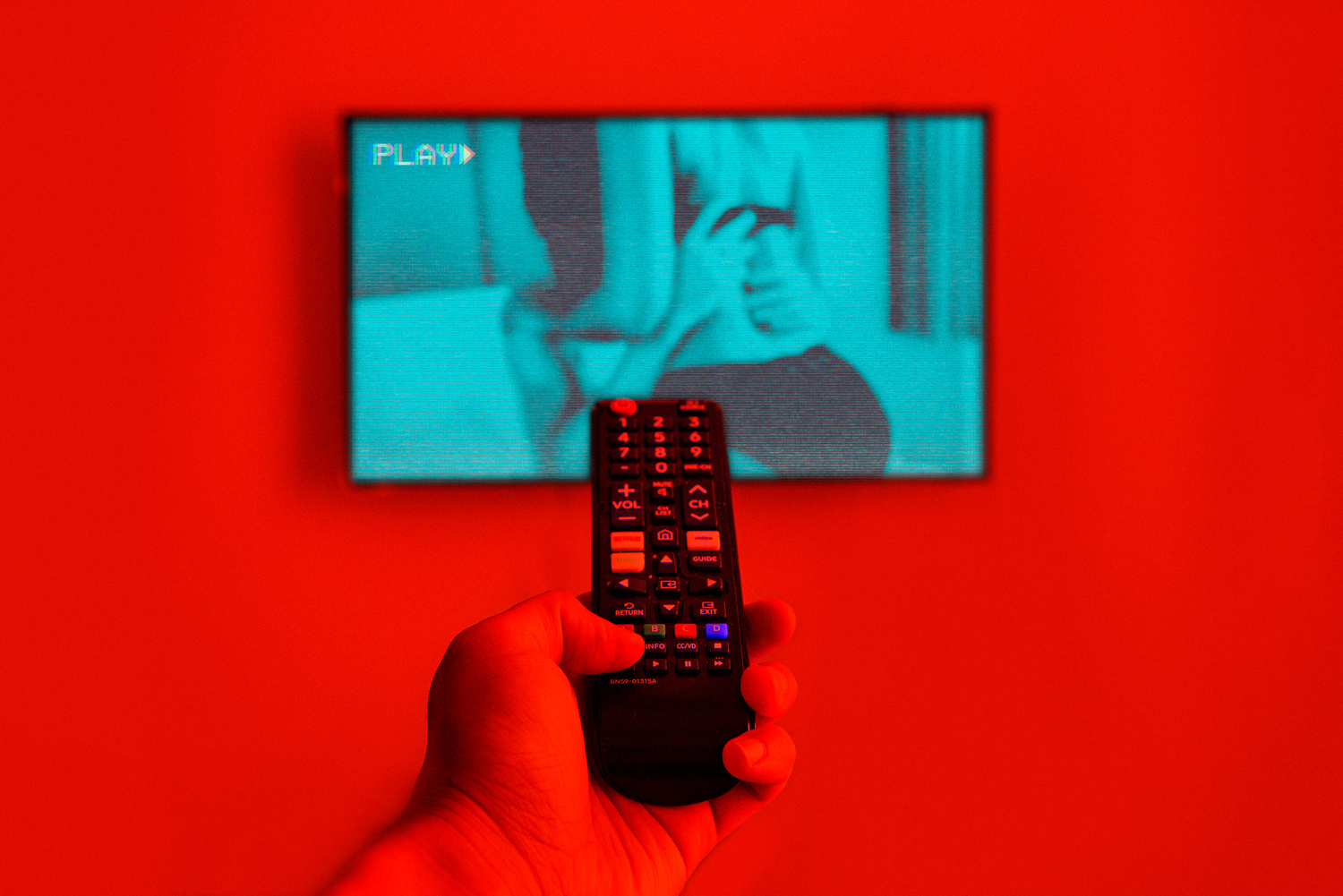 Hand holding a remote control with thumb over the rewind button as a raunchy scene is on the TV screen.