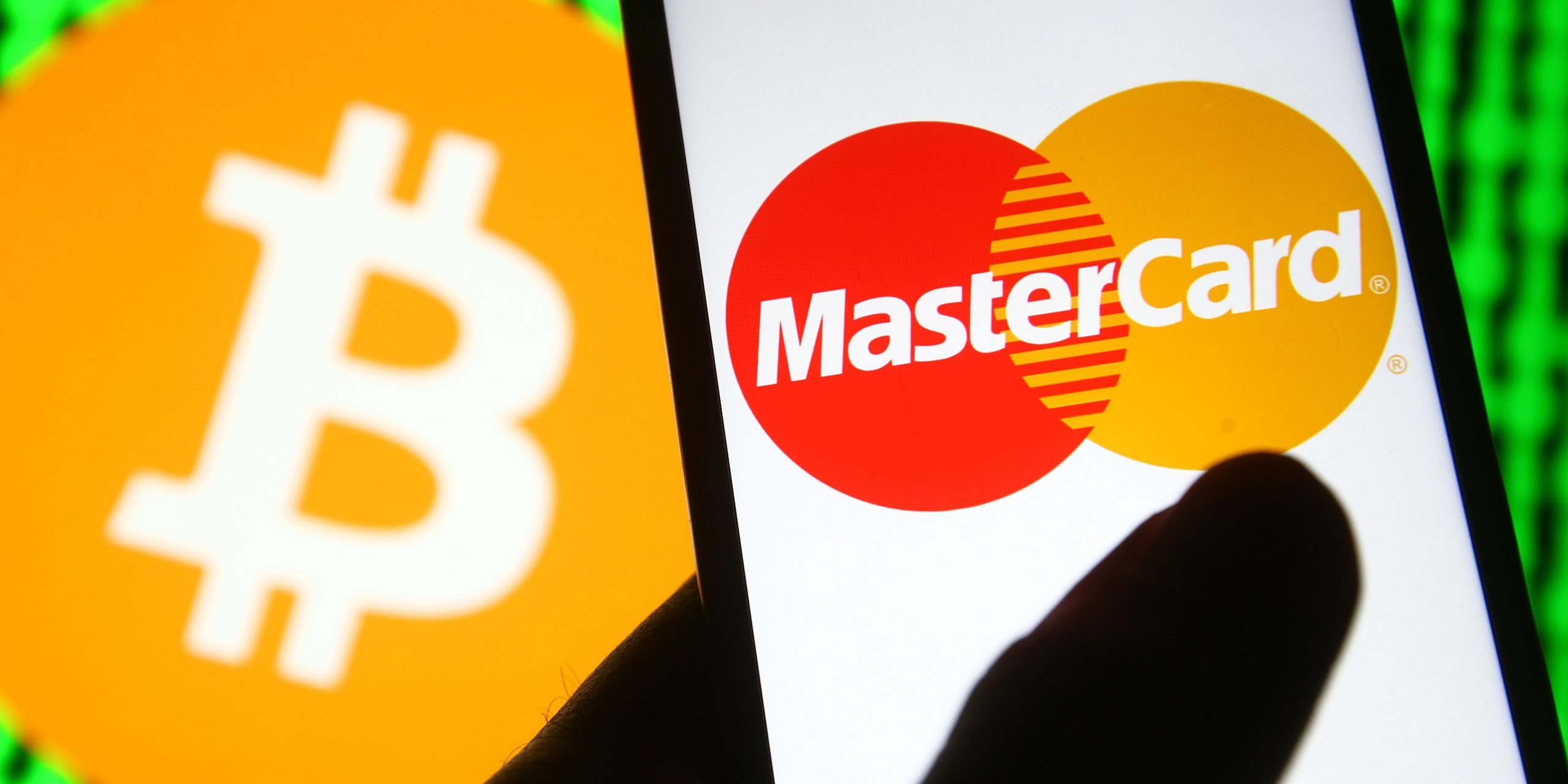 In this photo illustration a Mastercard logo is seen on a mobile phone in front of Bitcoin sign.