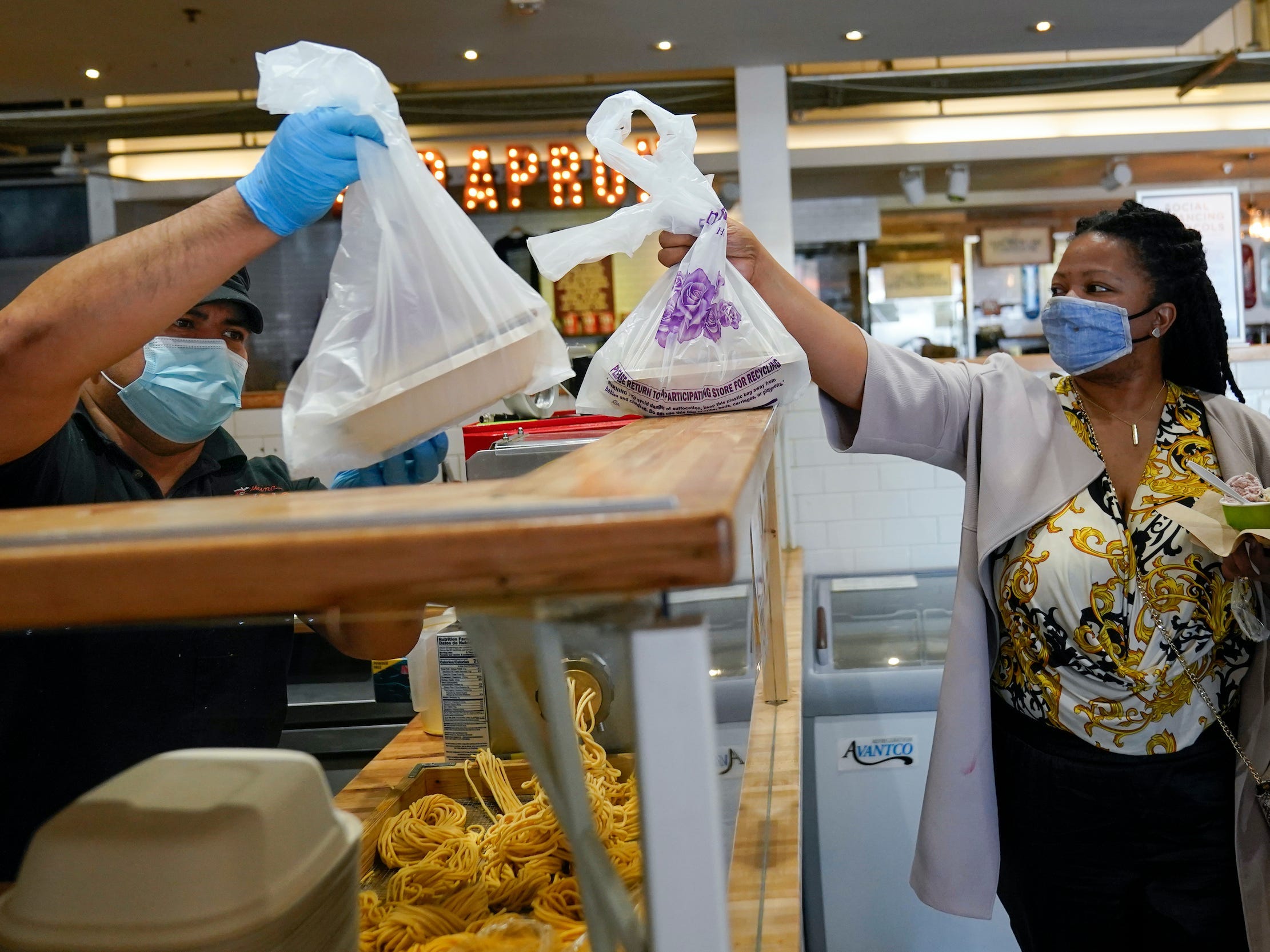 Man hands woman in face mask two bags of takeout food inside restaurant