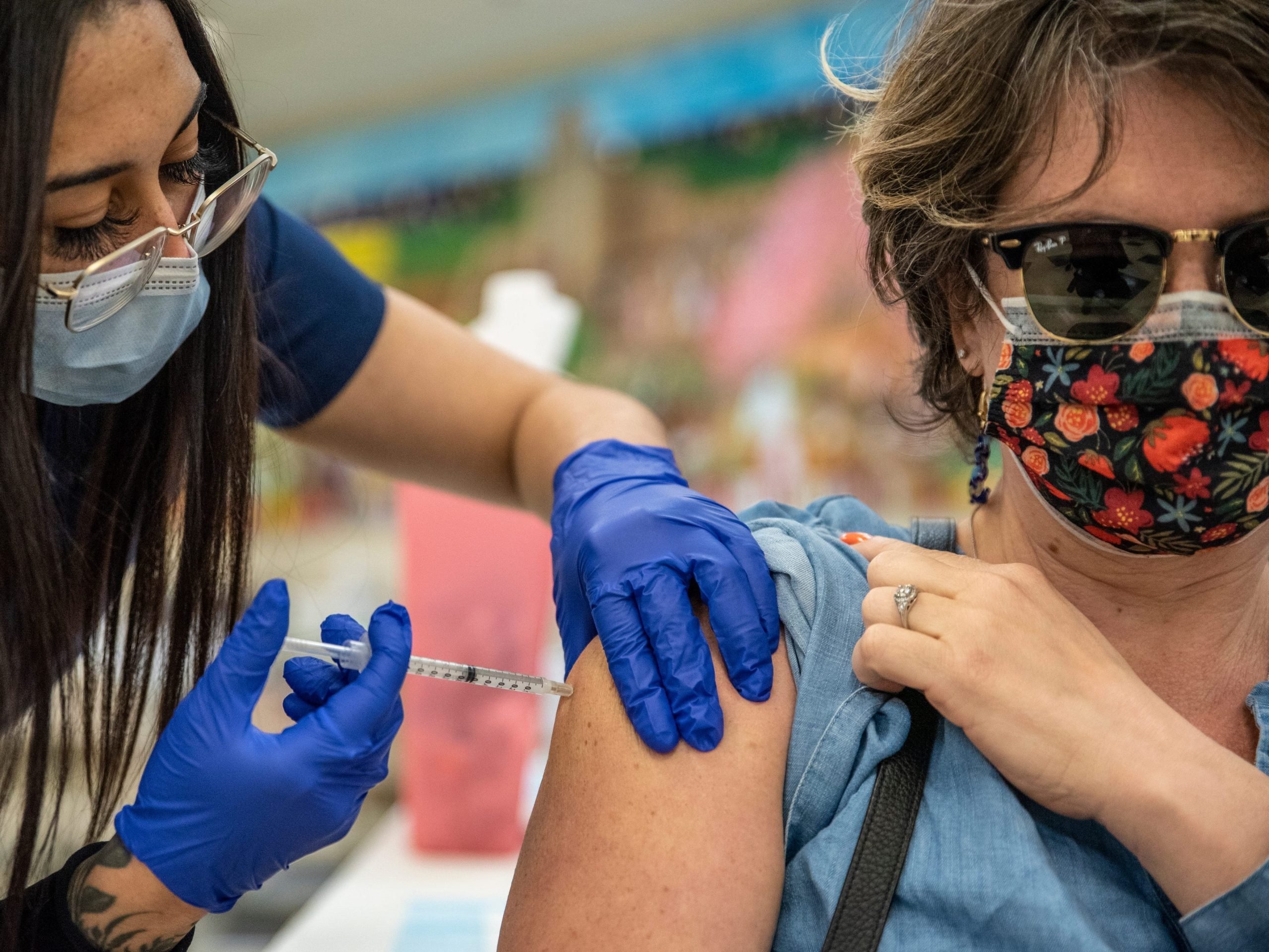 Women with mask and glasses administers COVID-19 vaccine to middle-aged women with sunglasses and patterned mask