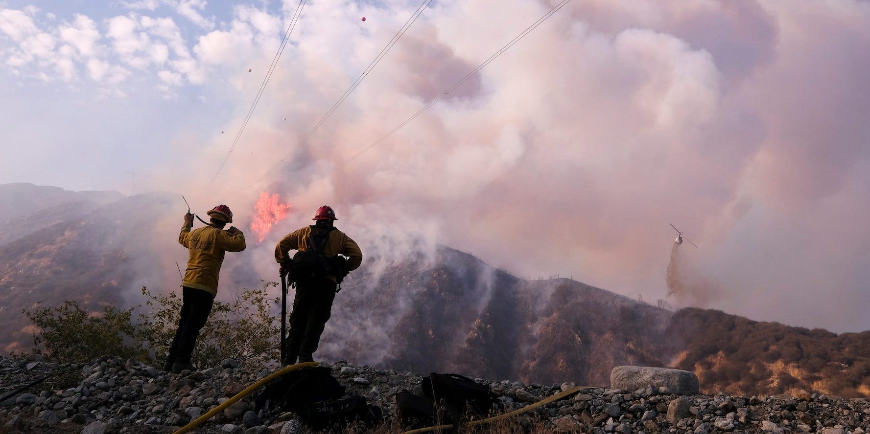 Firefighters watch a fire plume in the distance