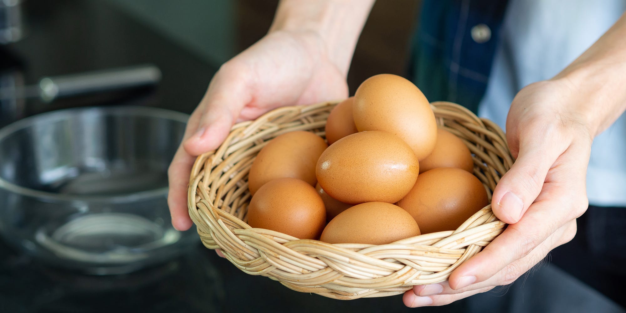A person holds a basket of brown eggs between their hands.