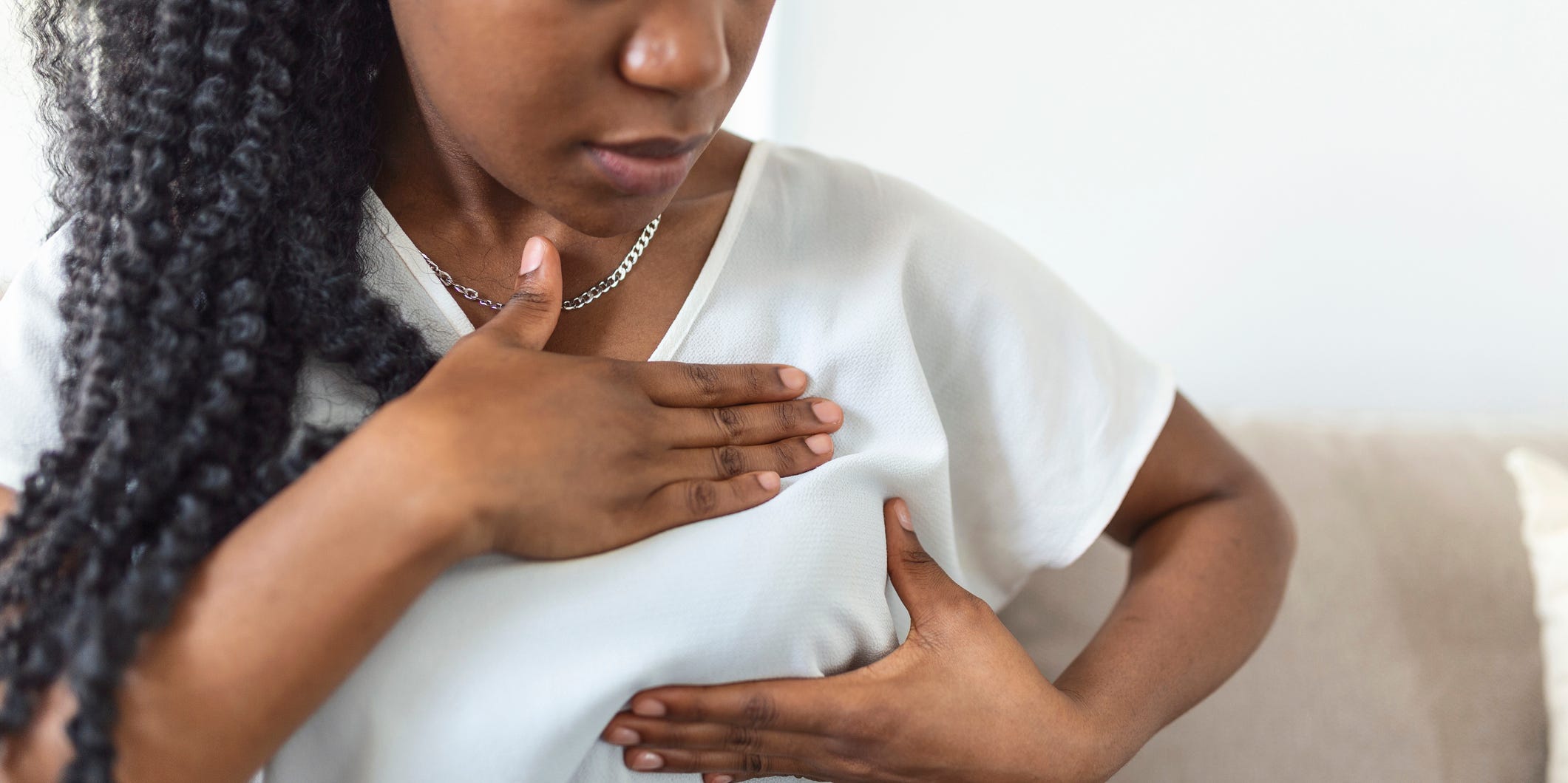 A Black woman holds her left breast as if checking for a lump.