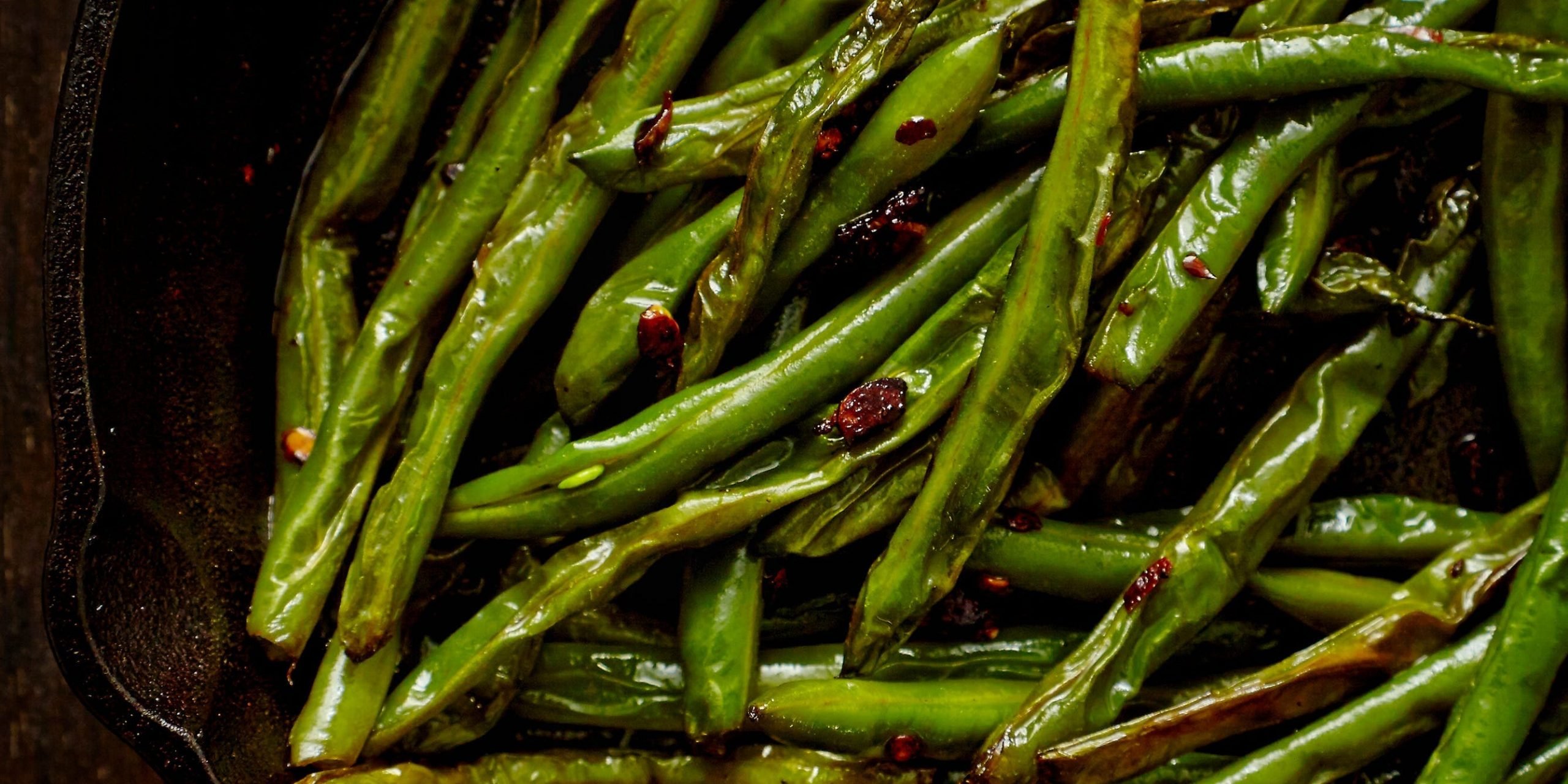 A top-down view of sautéed green beans in a cast iron skillet