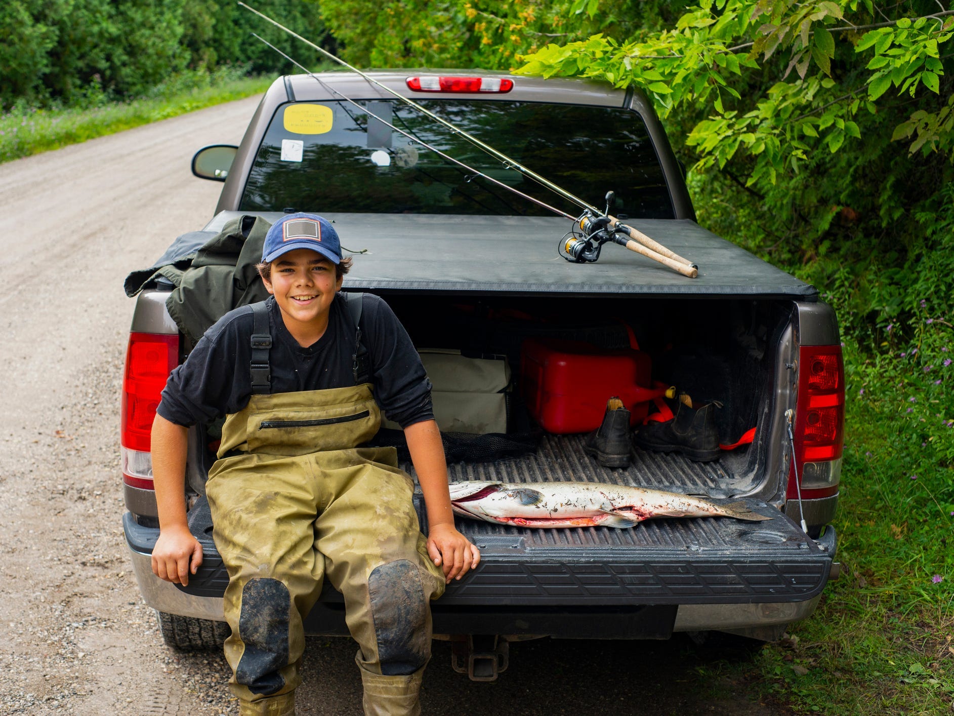 A young fisherman sitting on the back gate of a covered pickup truck