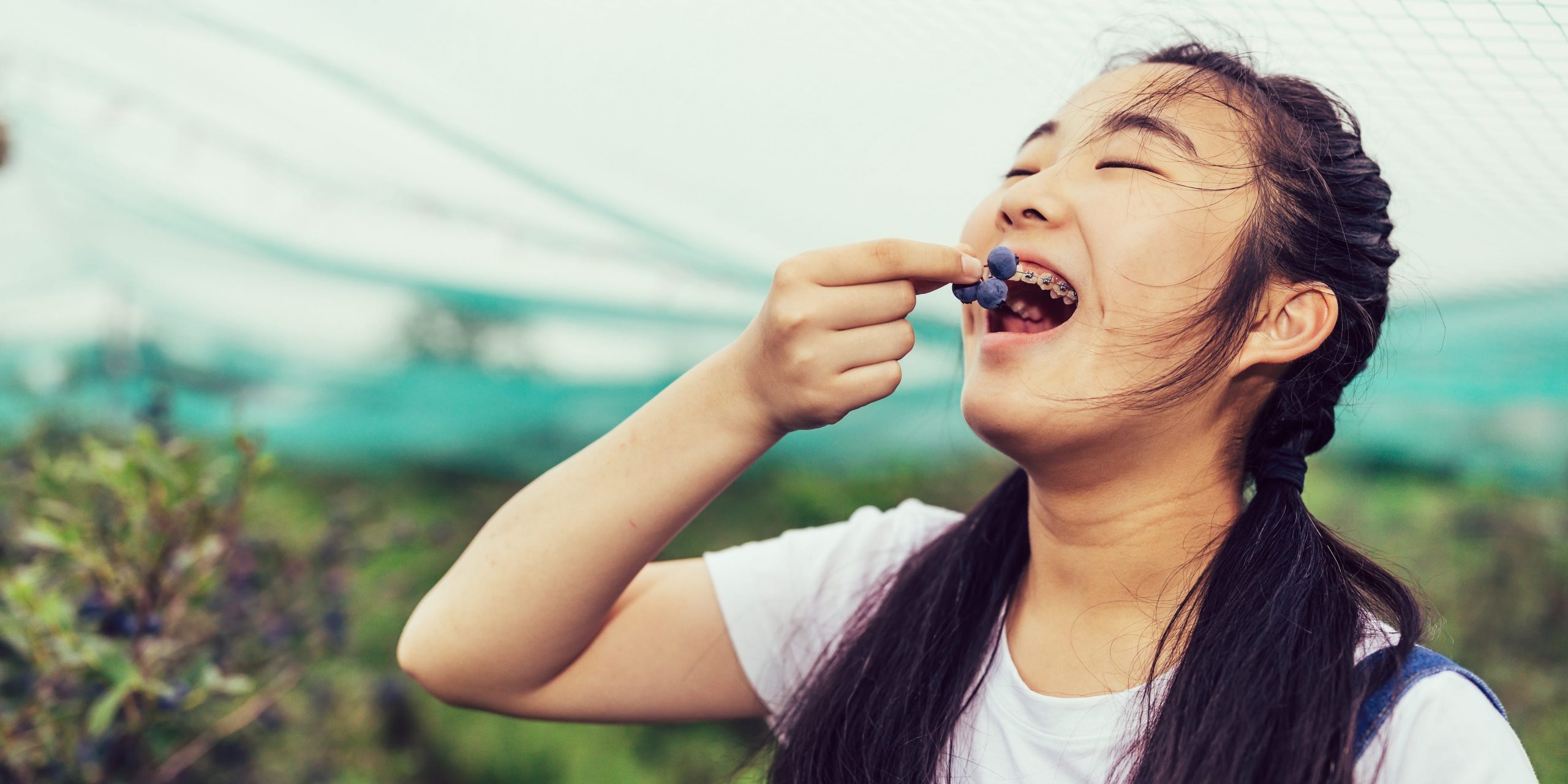 A teenager with braces eats fresh blueberries on a farm.