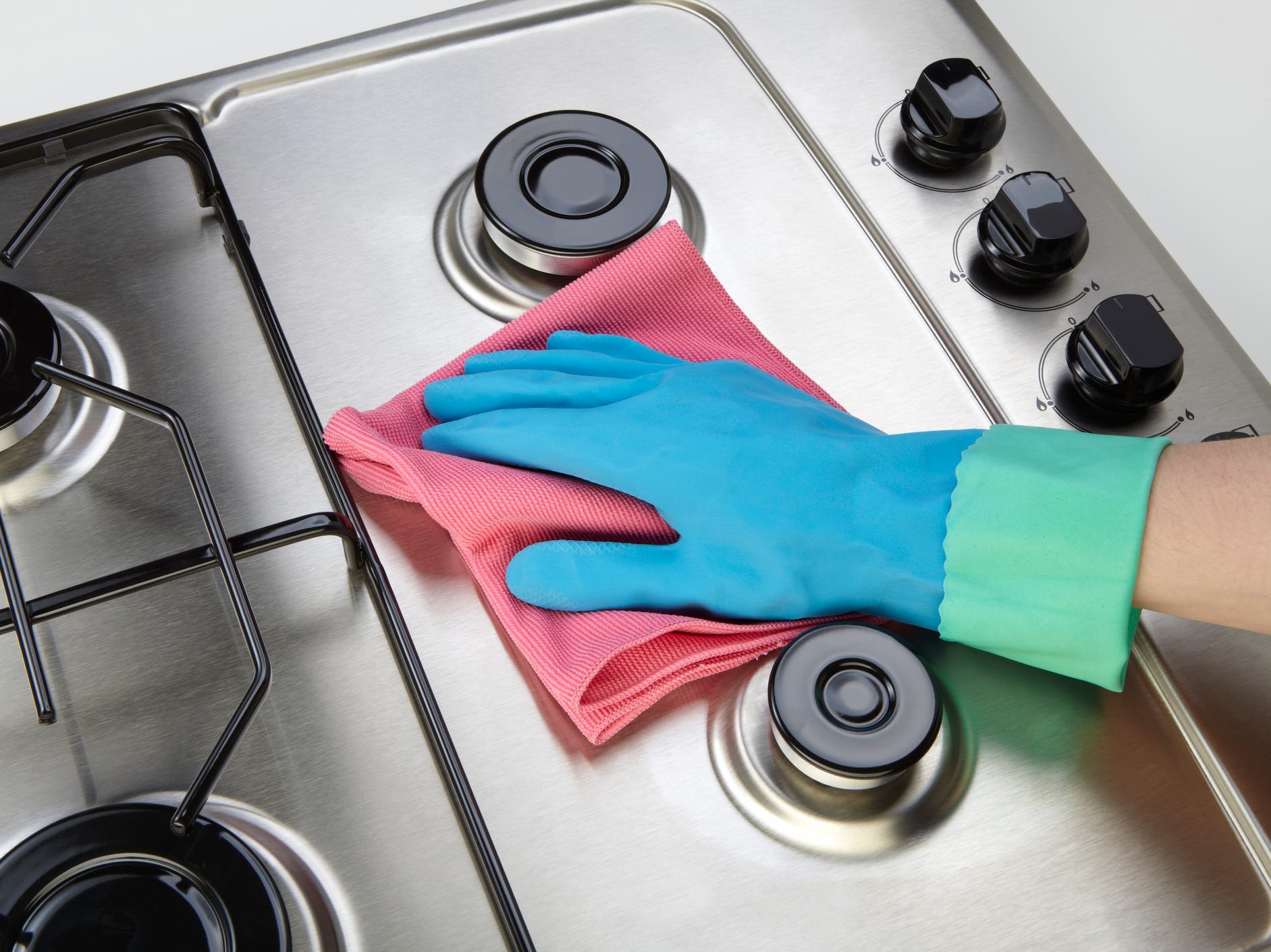 Woman cleaning set-top stove using microfiber rag and blue latex gloves.