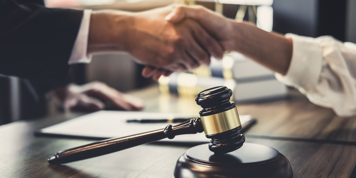 Close up of two people shaking hands near a legal pad and gavel.