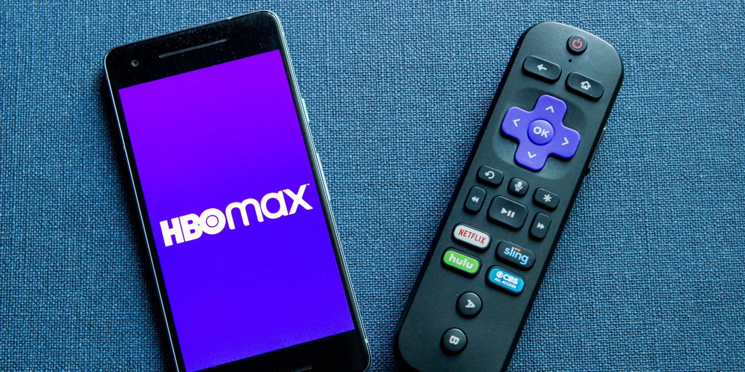 A smartphone displaying the HBO Max logo, sitting next to a Roku remote.