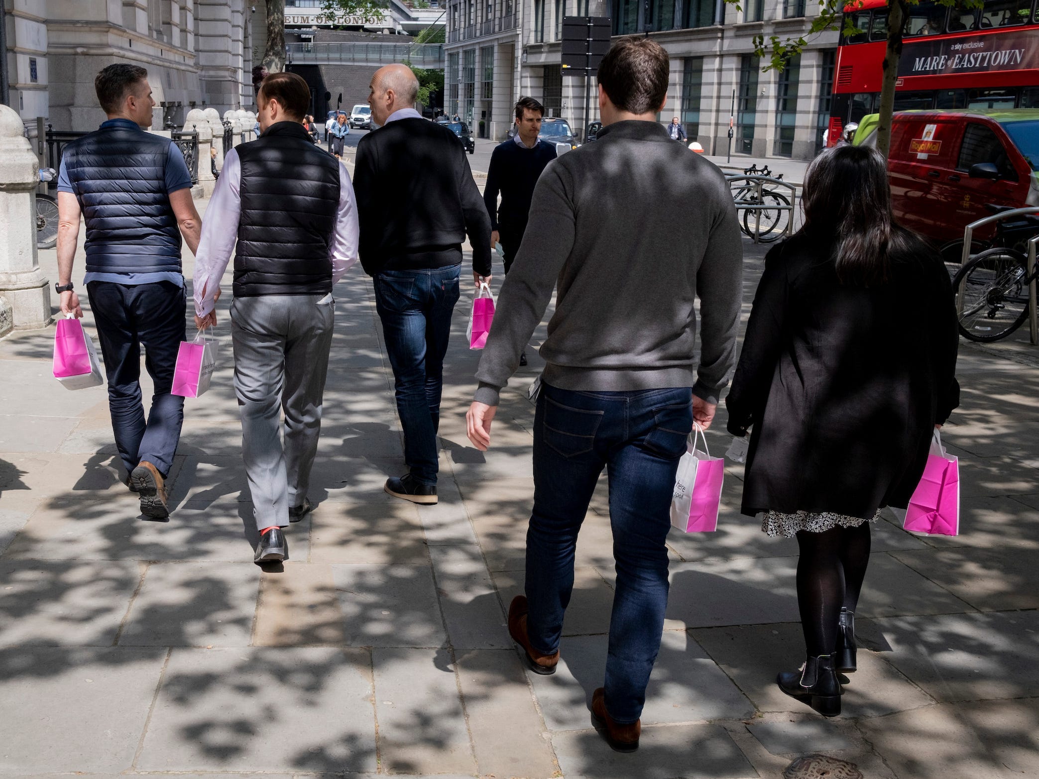 Group of office-workers carrying takeout lunch in pink paper bags walks down the street