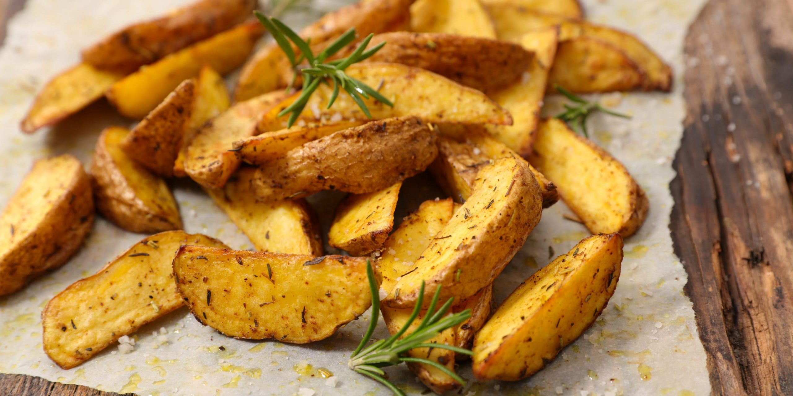 baked potato wedges arranged on a piece of wax paper with springs of rosemary