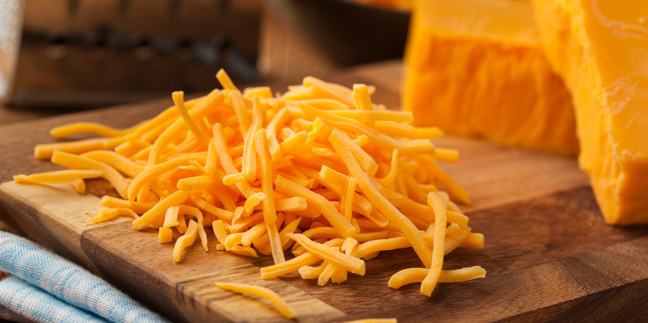 A pile of shredded cheddar cheese on a cutting board