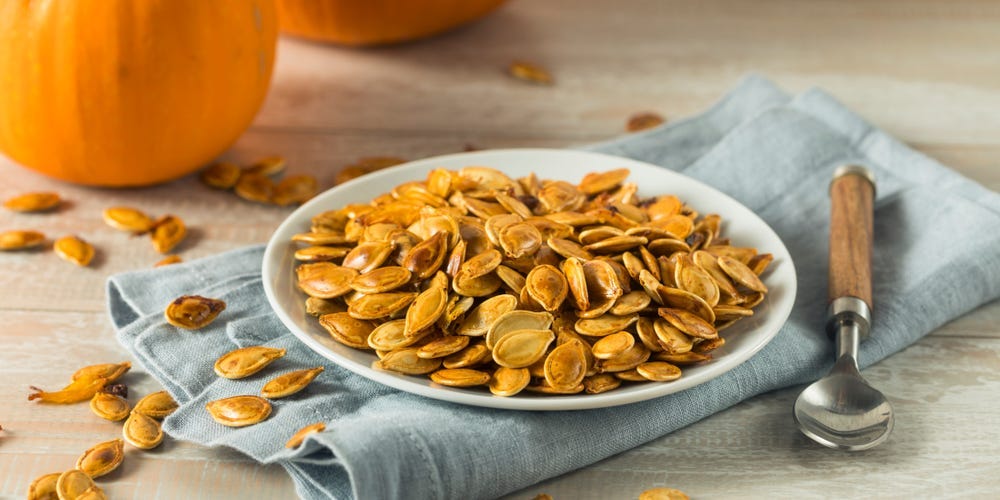 Roasted pumpkin seeds on a plate in front of pumpkins.