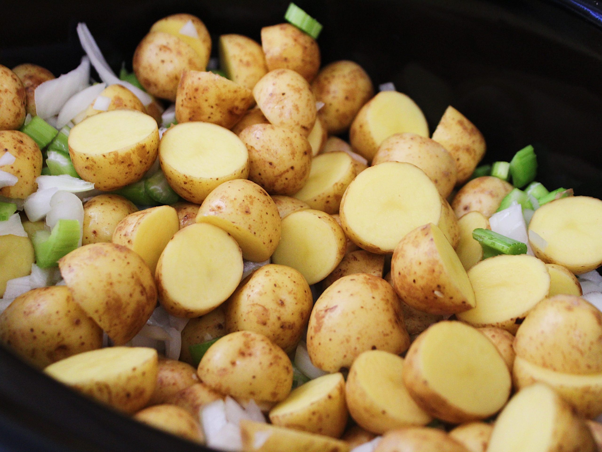 chopped potatoes celery and onions in a black slow cooker
