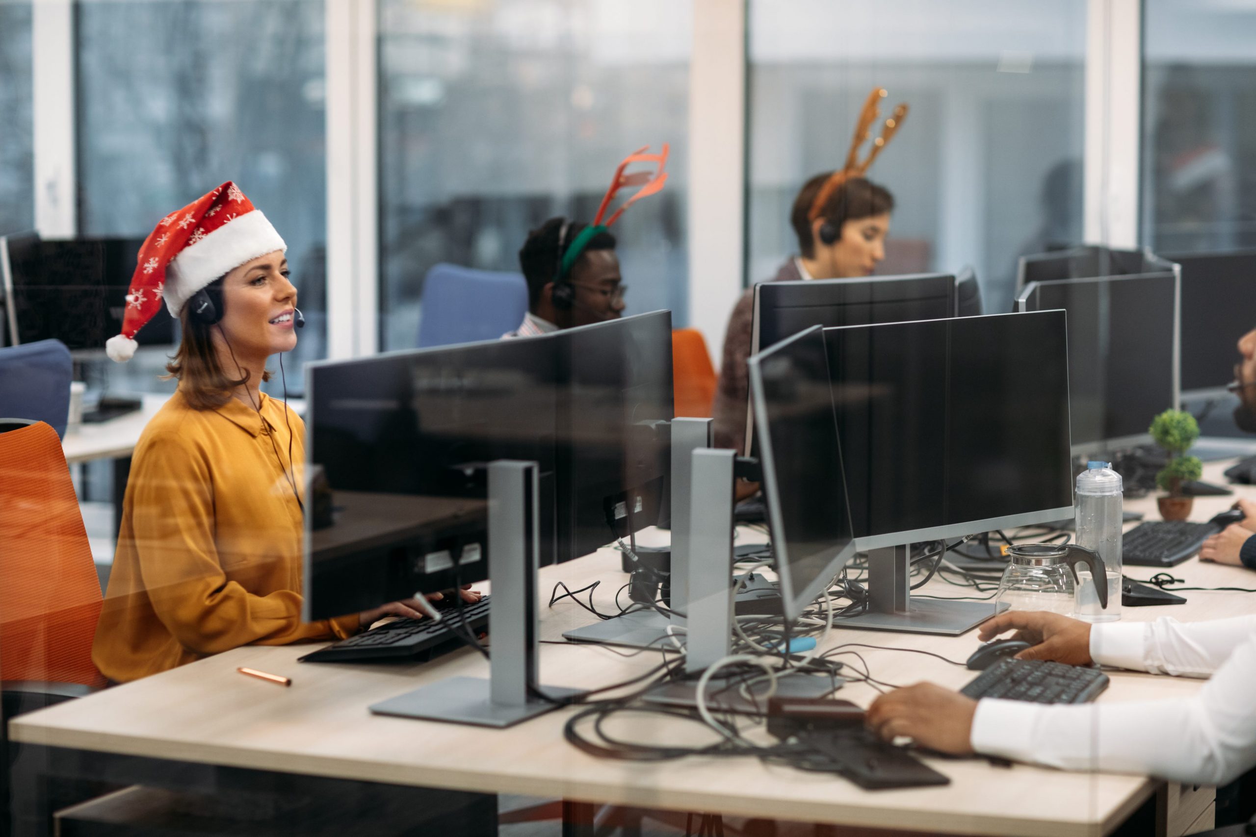 Workers in Santa hats and antlers work at desks