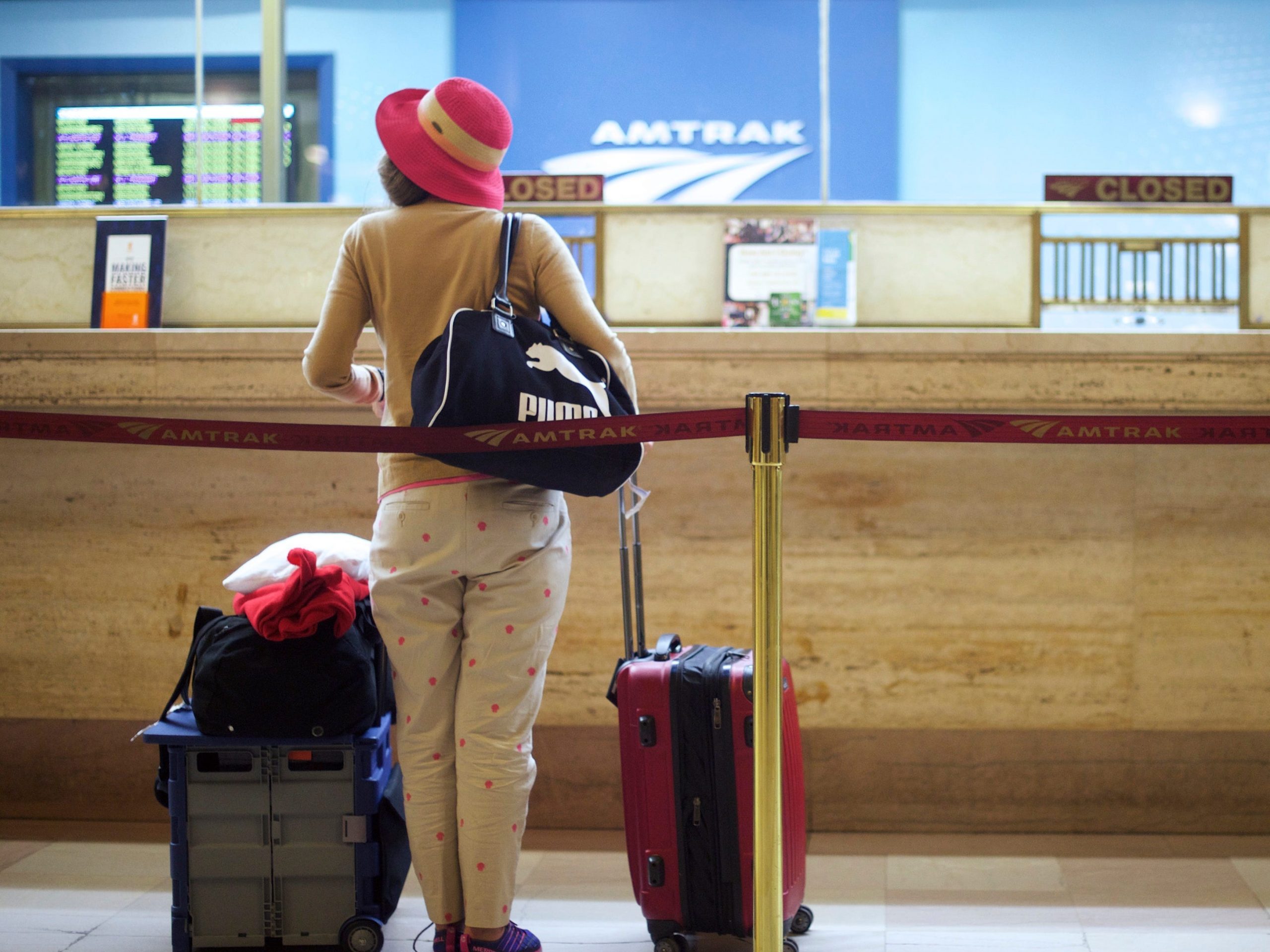 a woman standing in front of amtrak ticket booth with suitcases