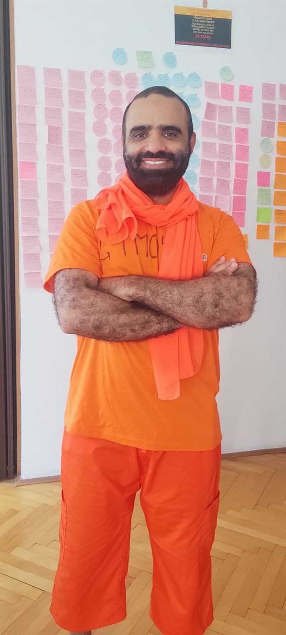 Mansoor Adayfi, wearing orange, stands in front of a wall of post-its.
