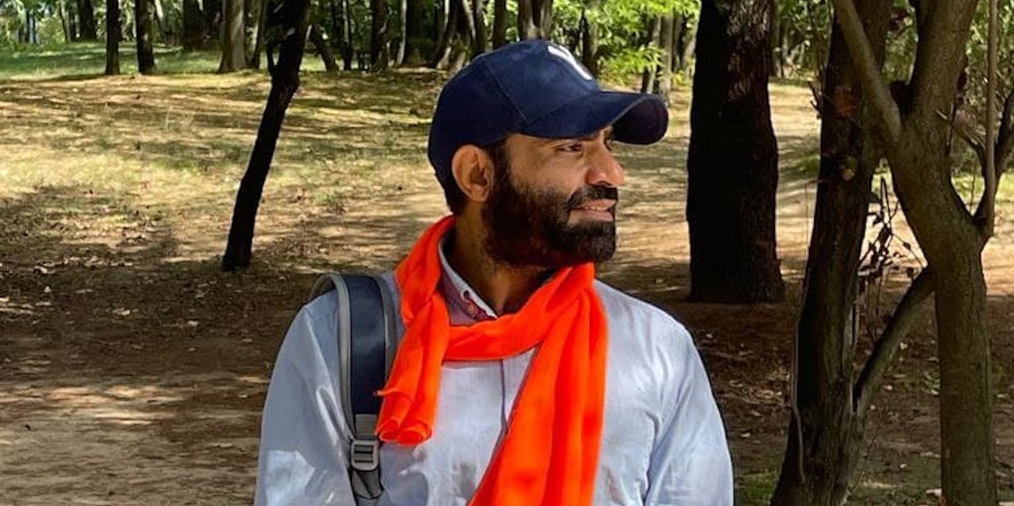Masoor Adayfi stands in front of trees with orange cloth around his neck
