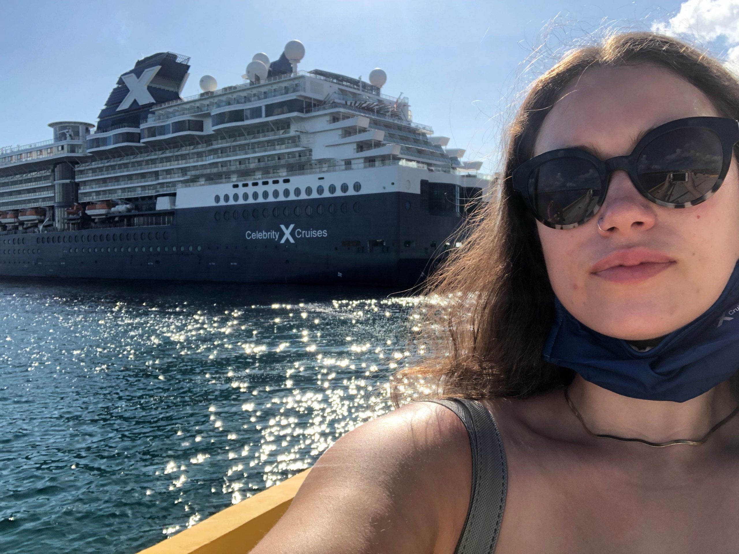 In a selfie, the author wears sunglasses and shows the navy blue and white cruise ship docked behind her.