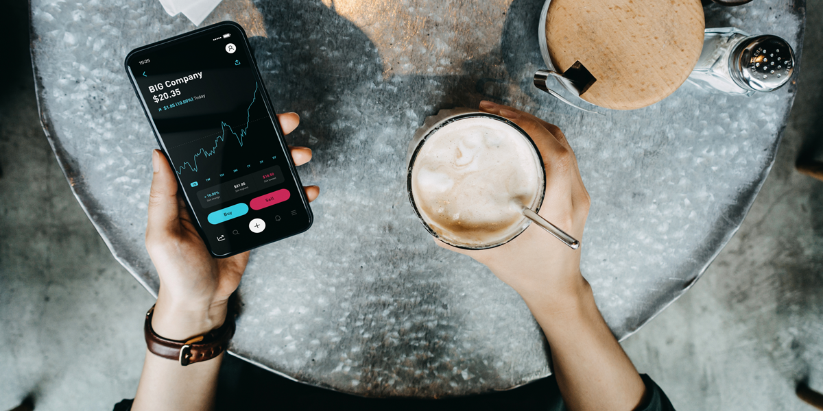 Overhead view of a woman on a coffee break while checking financial stock market data on a smartphone in a cafe.