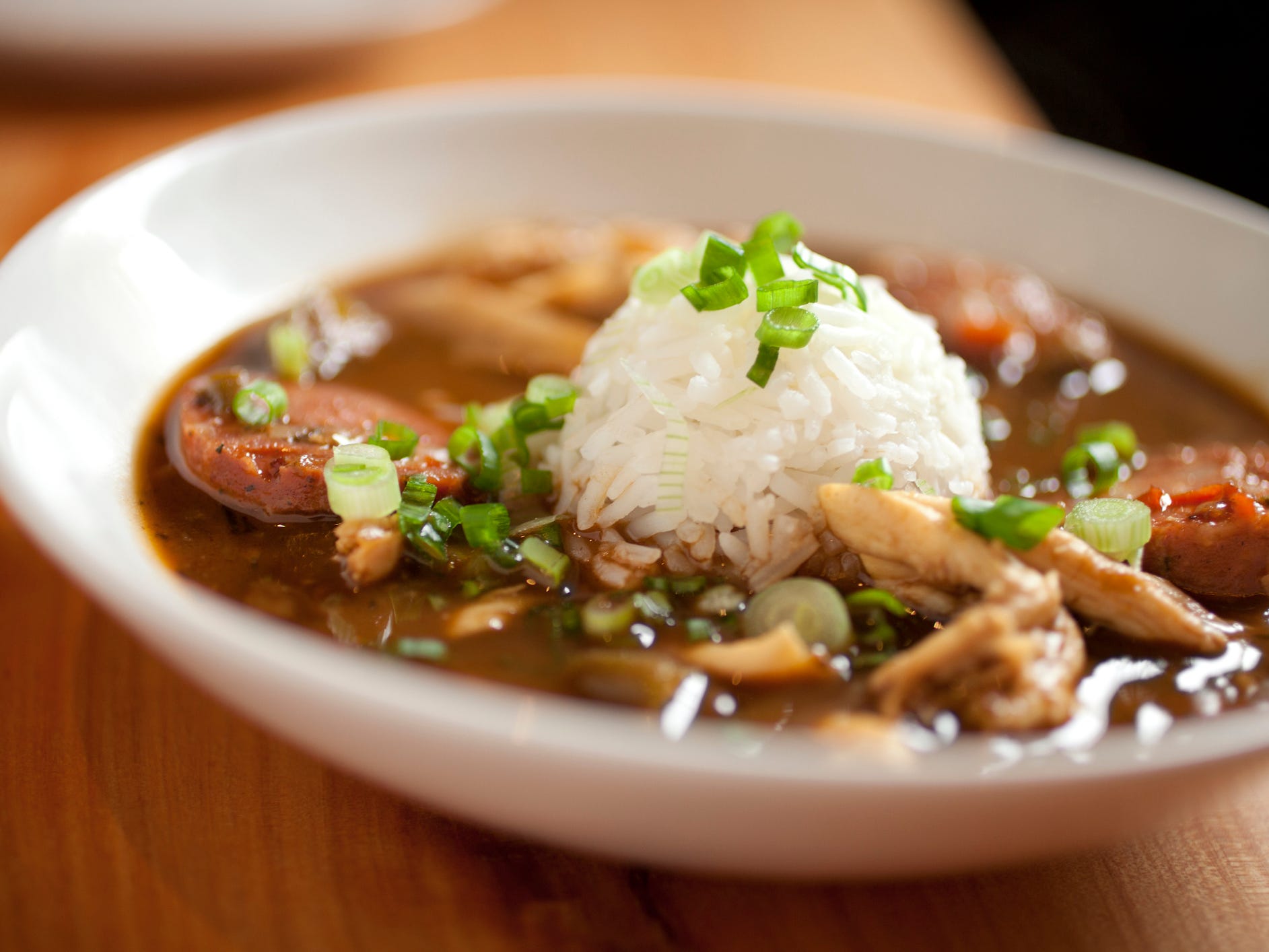A bowl of sausage gumbo topped with a scoop of white rice and scallions