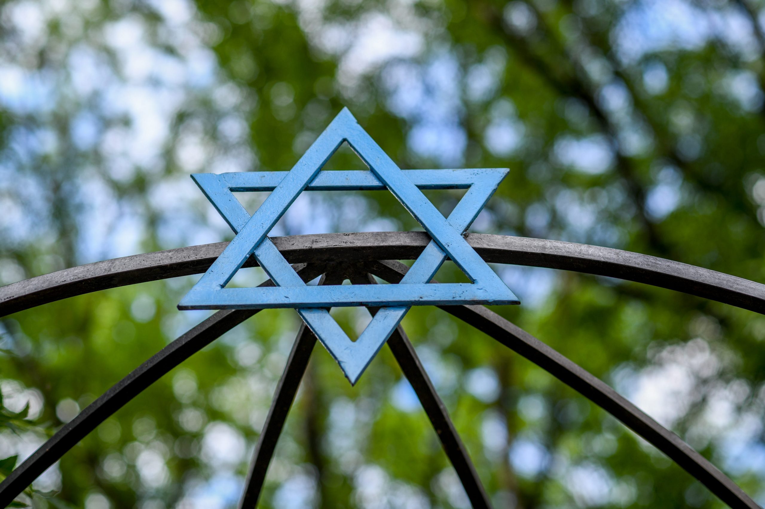 A blue Star of David over a gate in Poland with trees and the sky in the background behind it