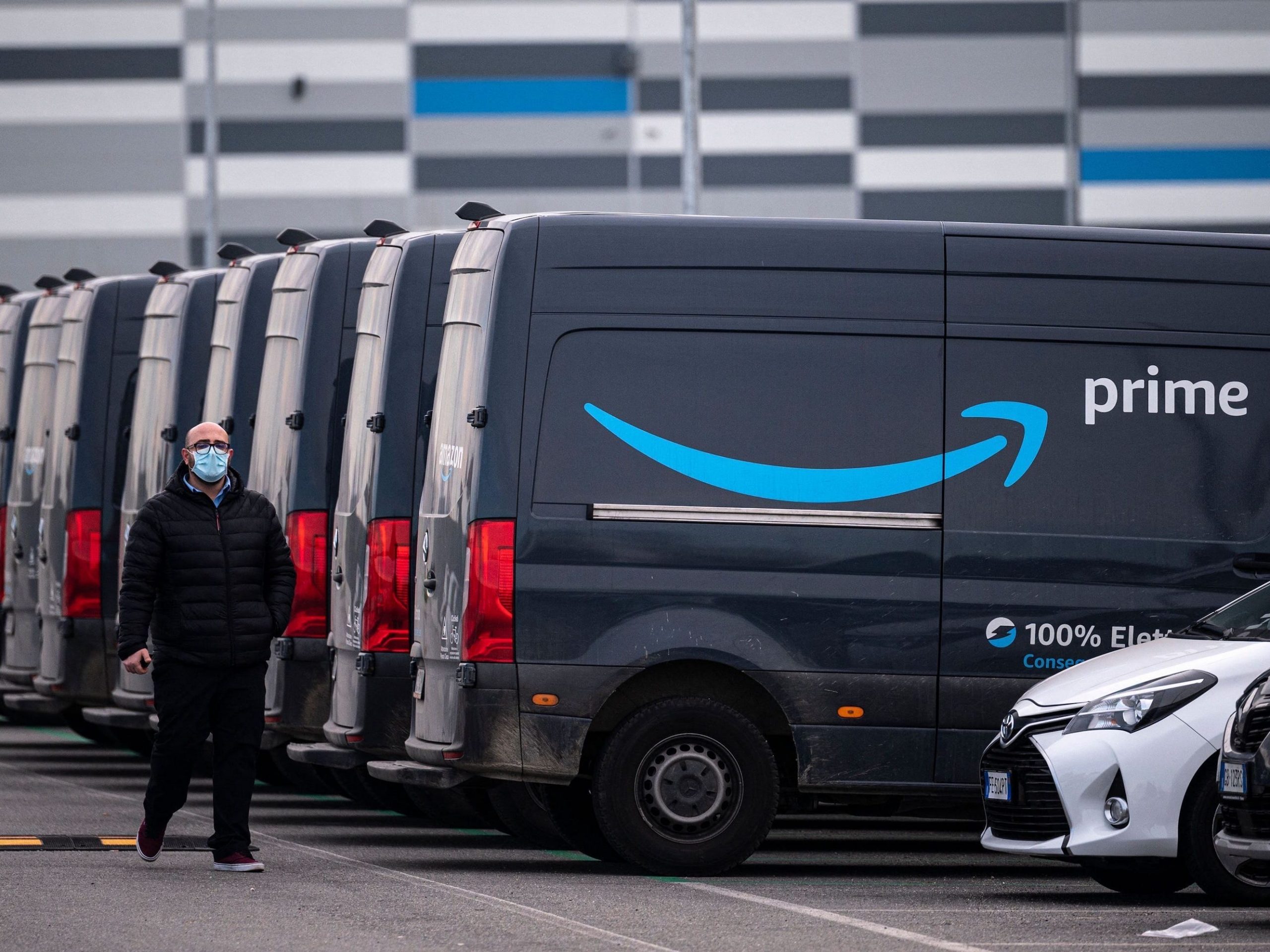 An Amazon employee walks by an Amazon Prime delivery truck in the company's premises in Brandizzo, near Turin, March 22, 2021