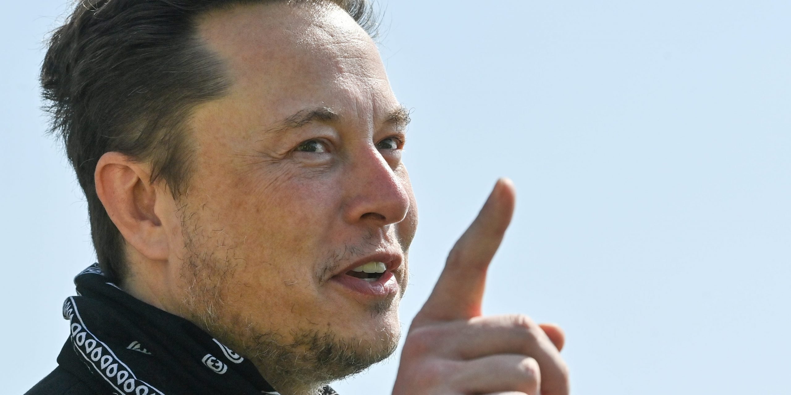 Tesla CEO Elon Musk points a finger upward while wearing a black bandana around his neck