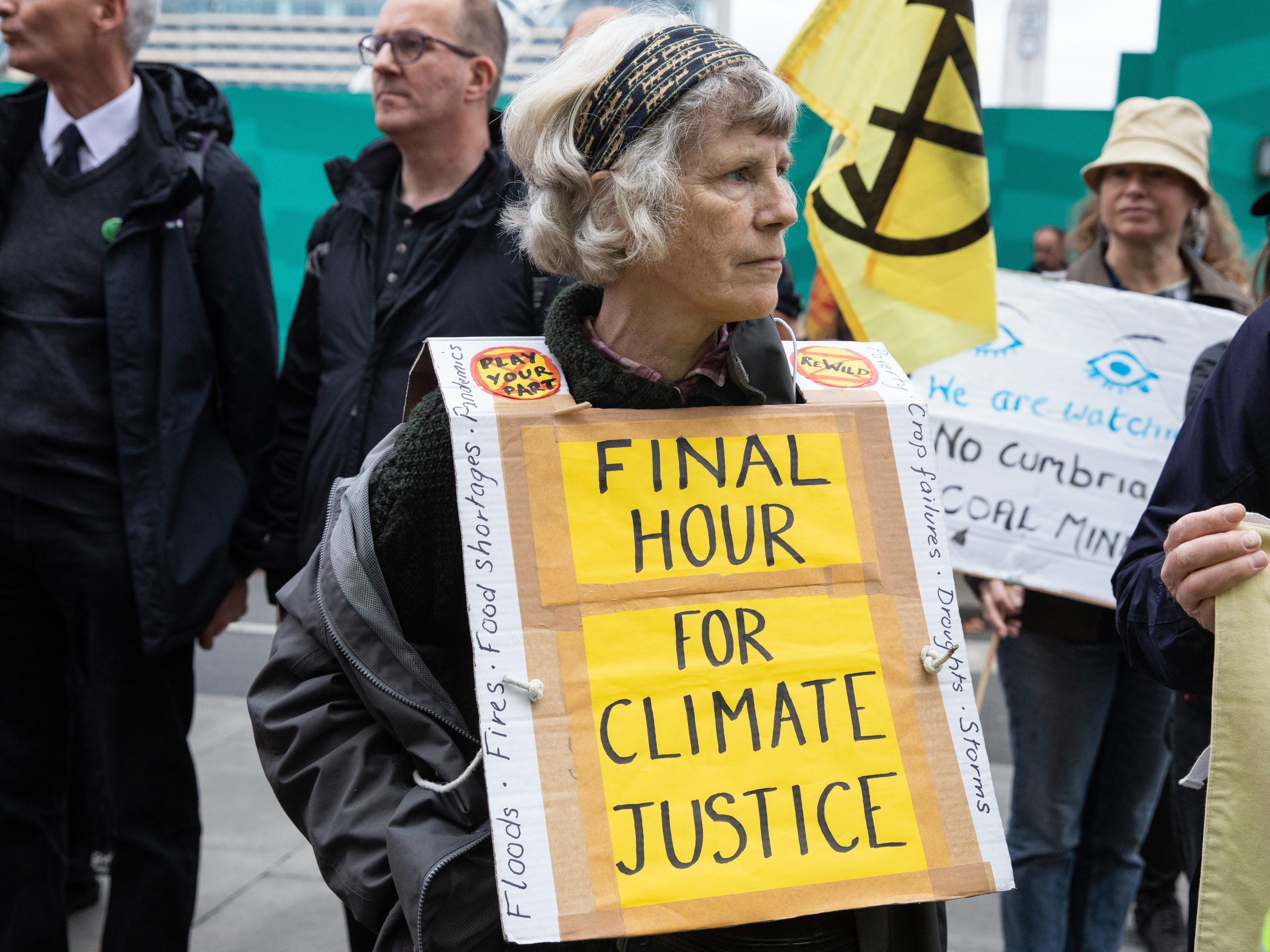 Older woman protesting at COP26 with sign around her neck that says, "Final hour for climate justice."