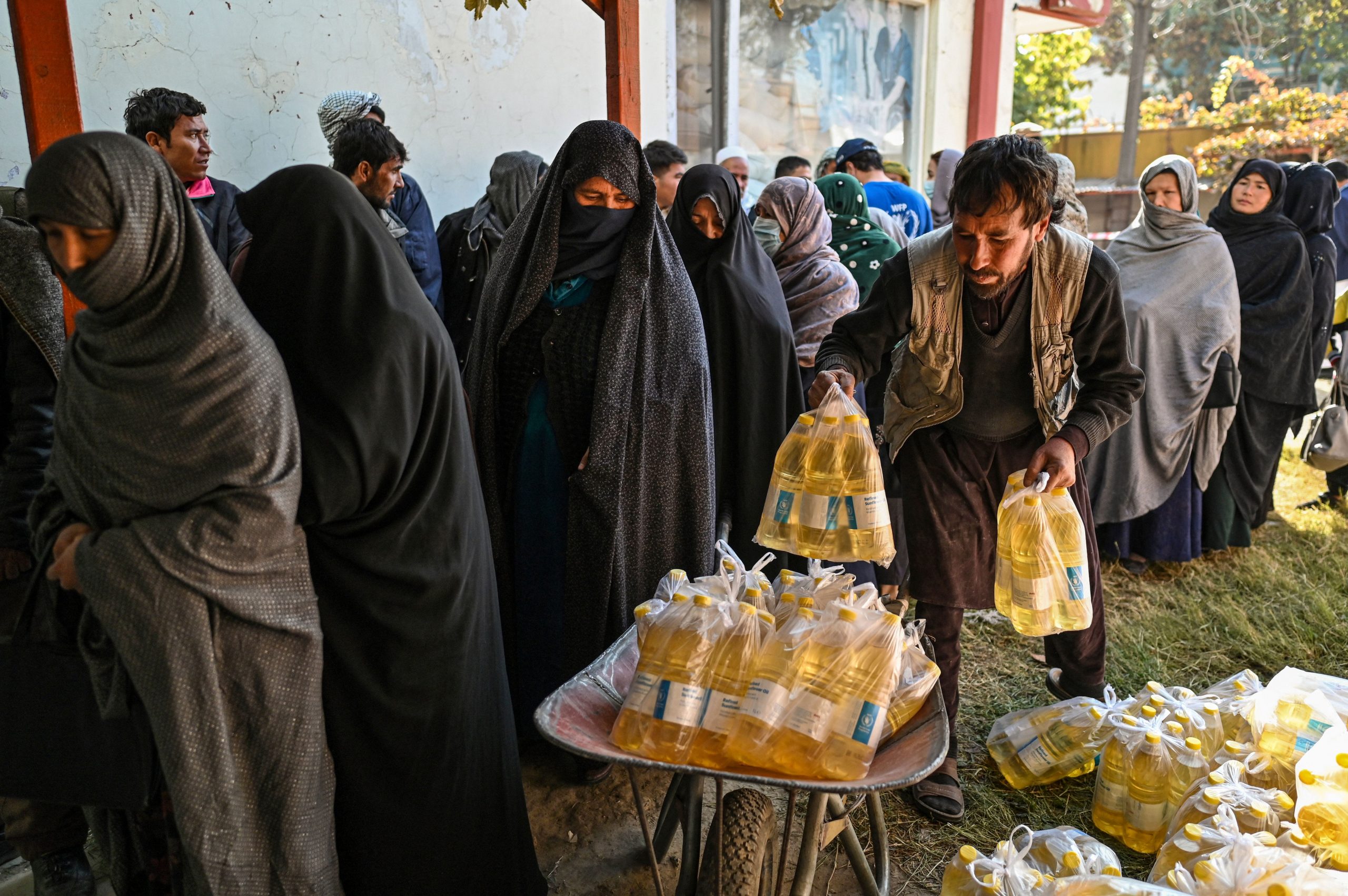 Half a dozen veiled and covered women stand in line as several men with uncovered faces handle food donations.