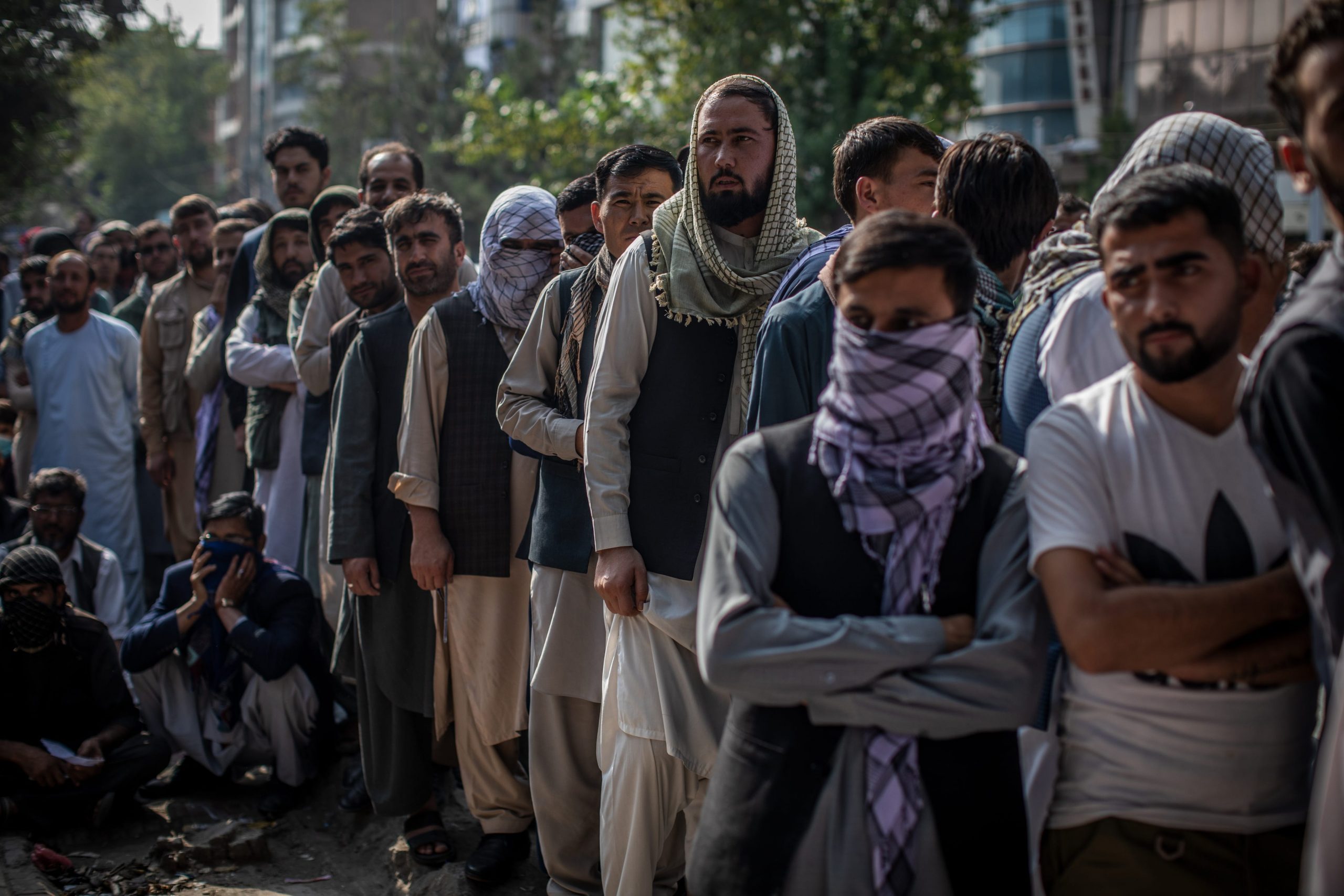 A long row of men stand in line outdoors in Kabul, Afghanistan.