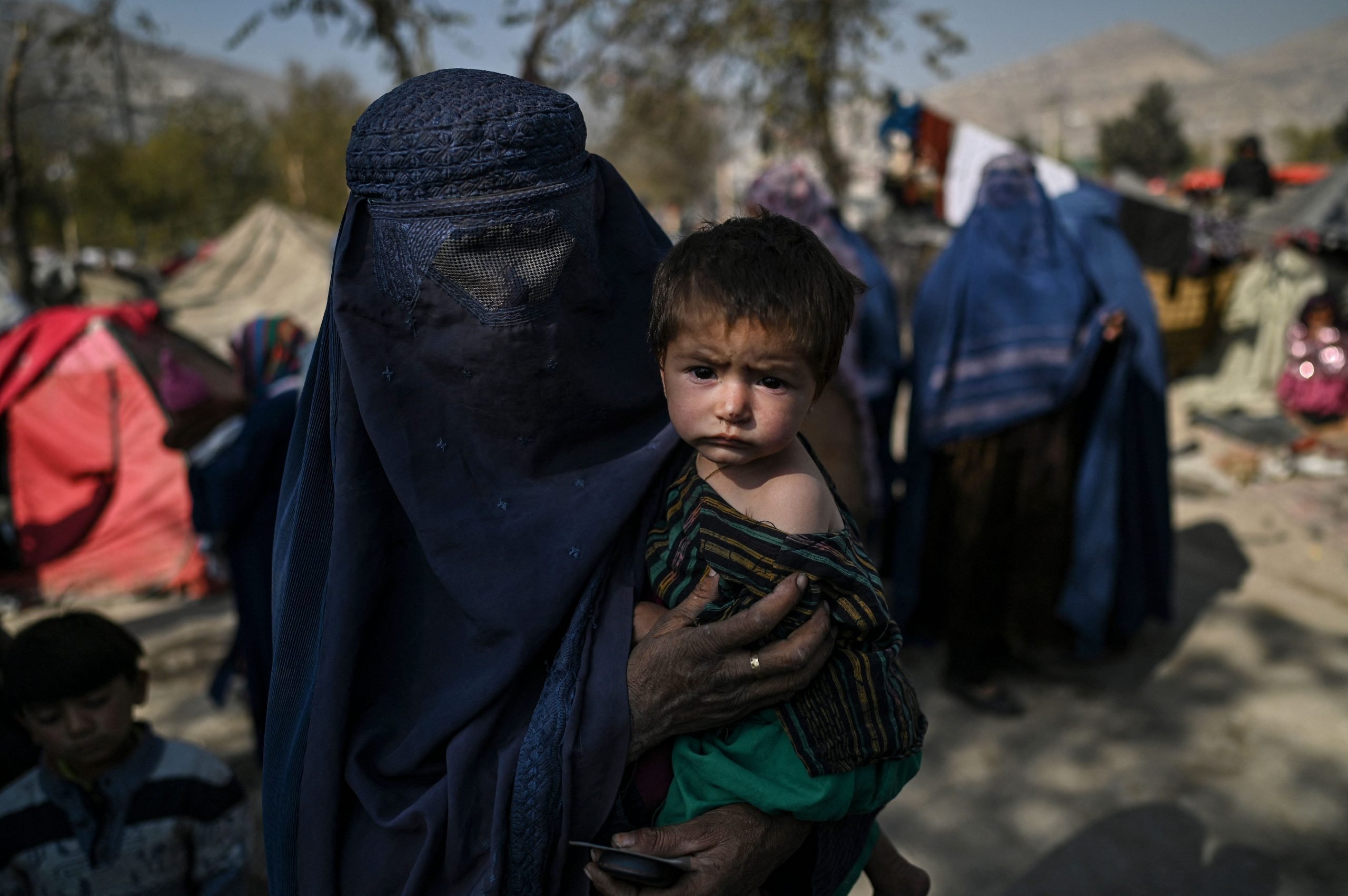 A woman with her face covered holds a small child as others walk by.