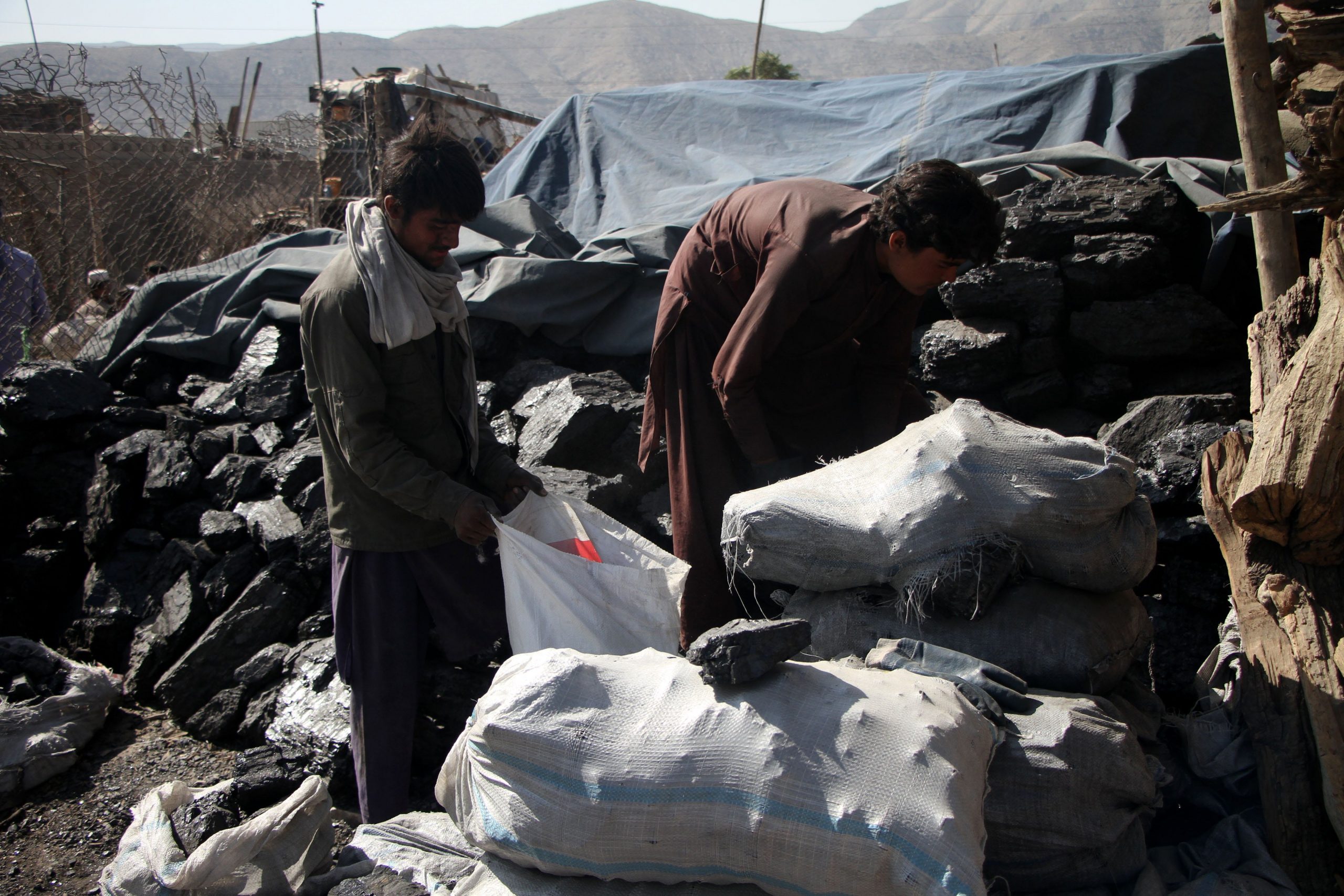 Two men are seen working amid piles of coal.