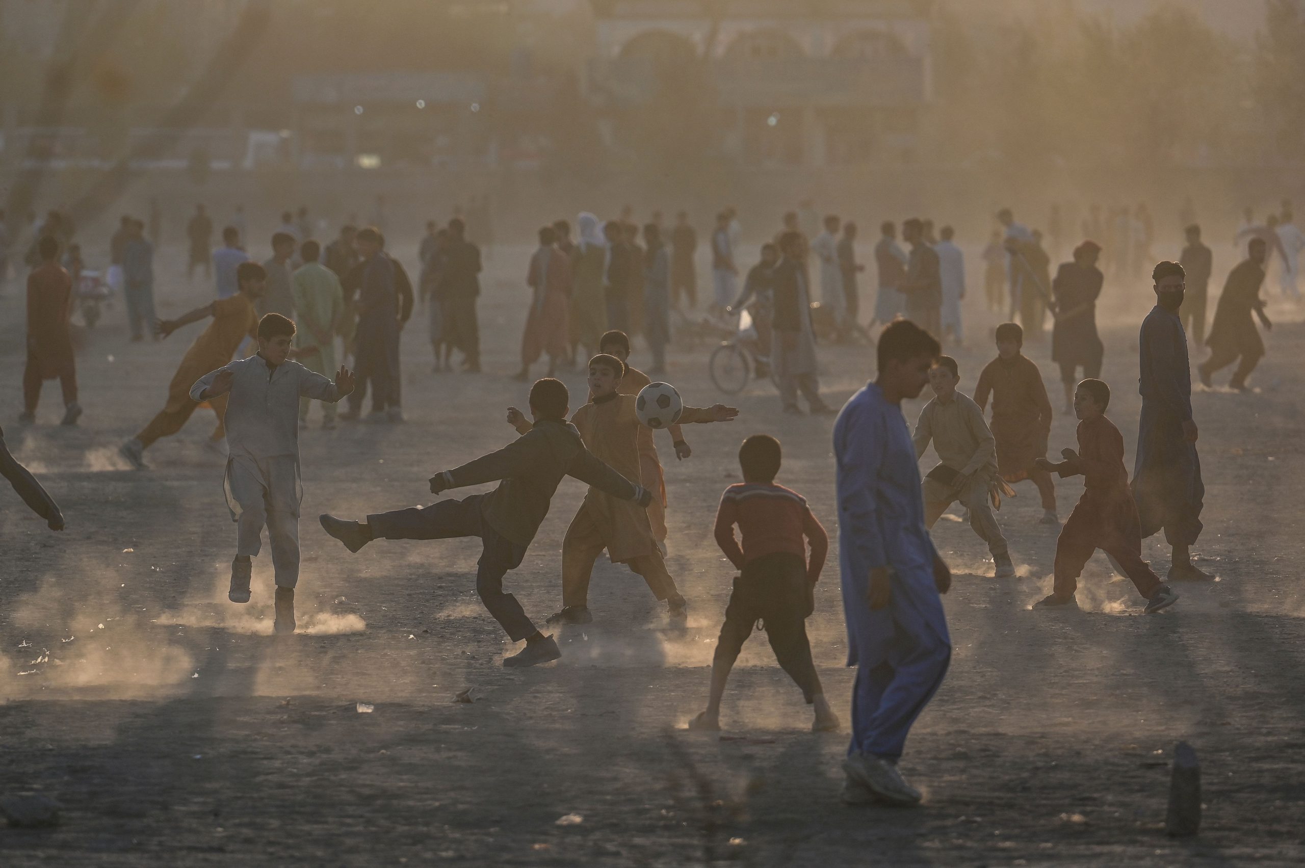 A crowd of boys are seen playing soccer in a crowded, open park.