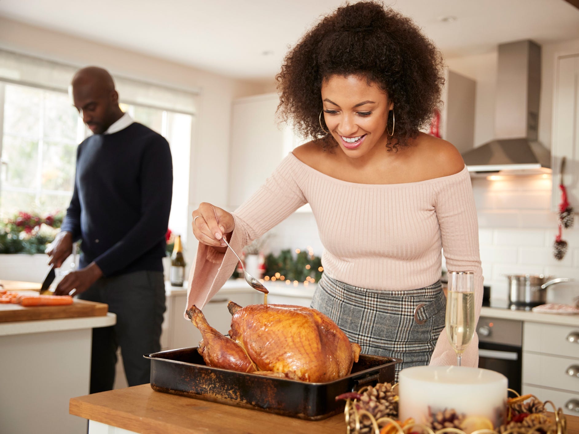 A woman using a spoon to baste a turkey
