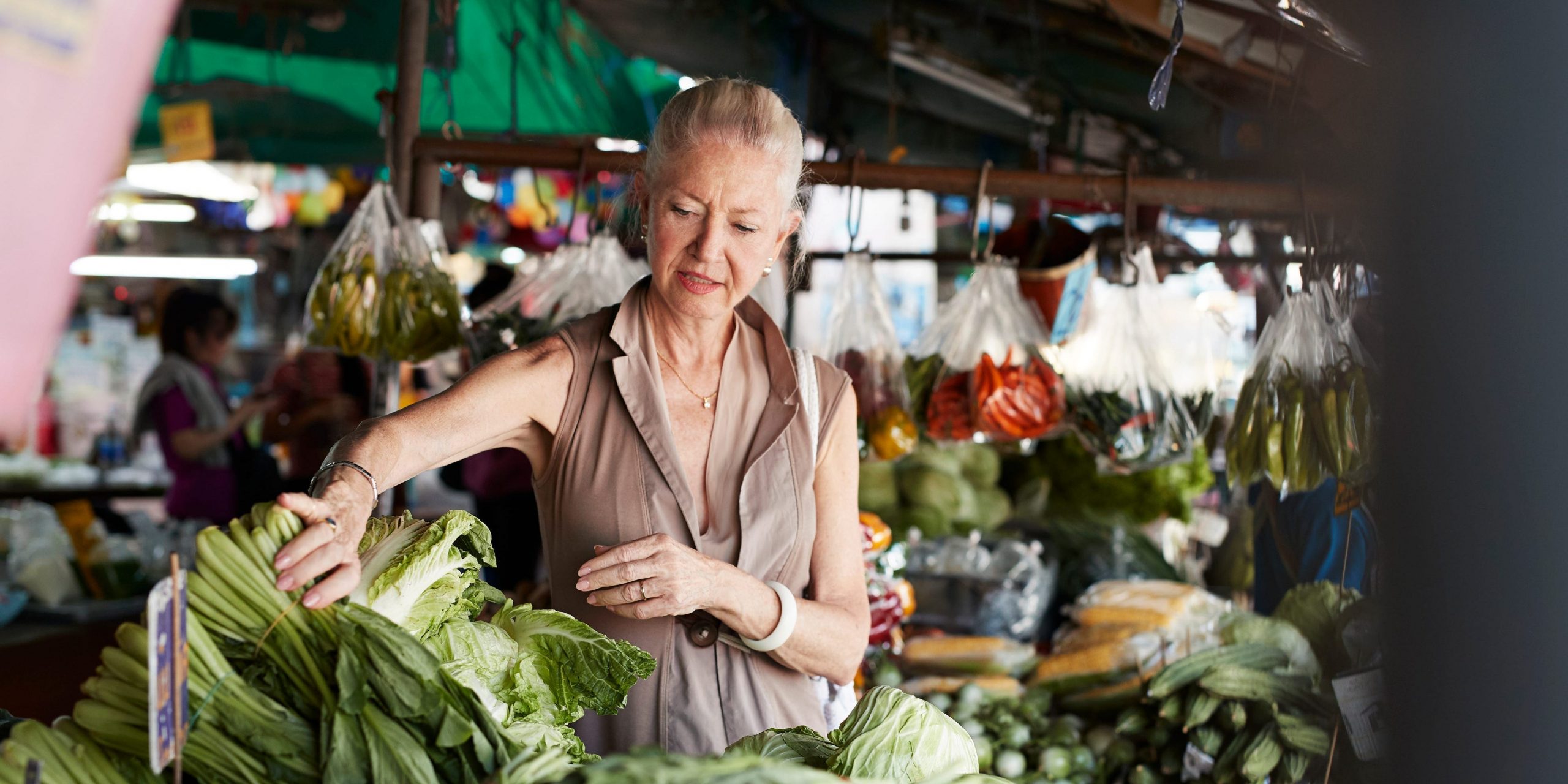 A middle-aged woman picks up leafy green vegetables at a farmer's market.
