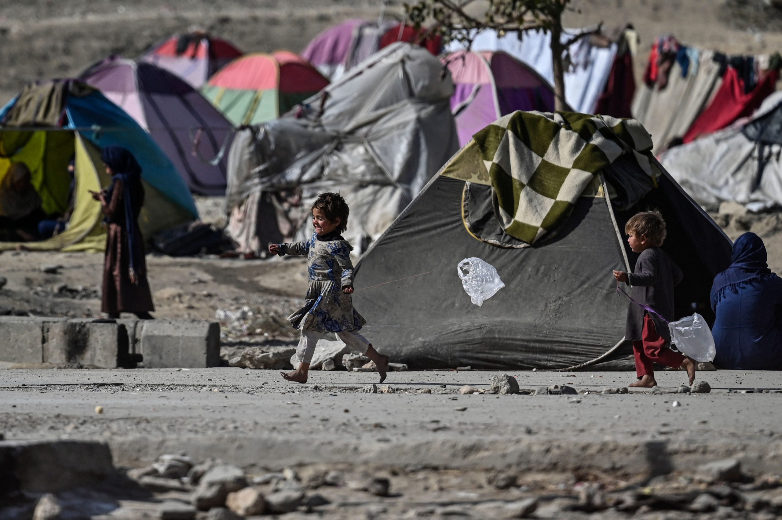 Children are seen running amid a cluster of tents and dirt pathways.